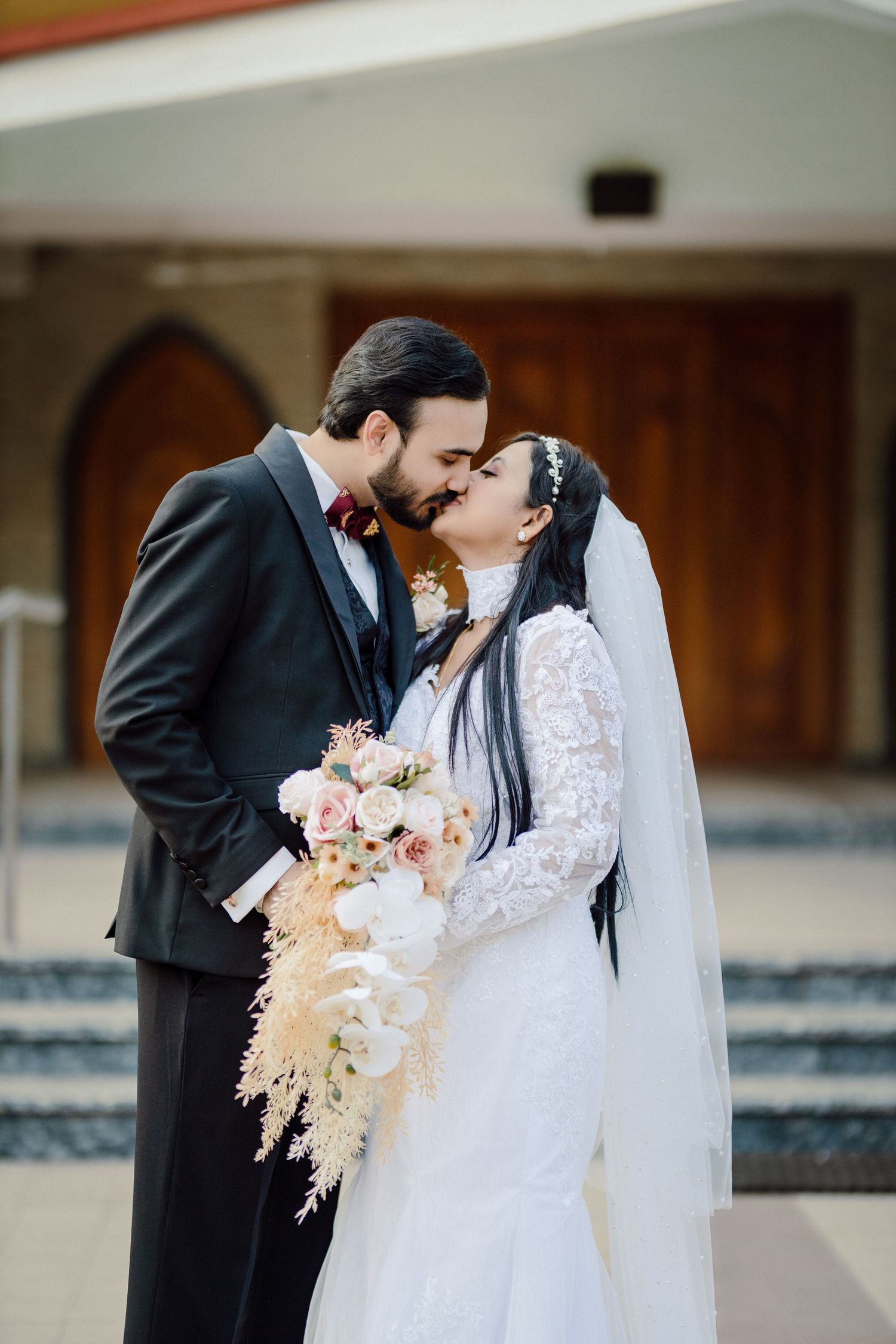 Romantic wedding portrait of couple with cascading bouquet against wooden church doors.