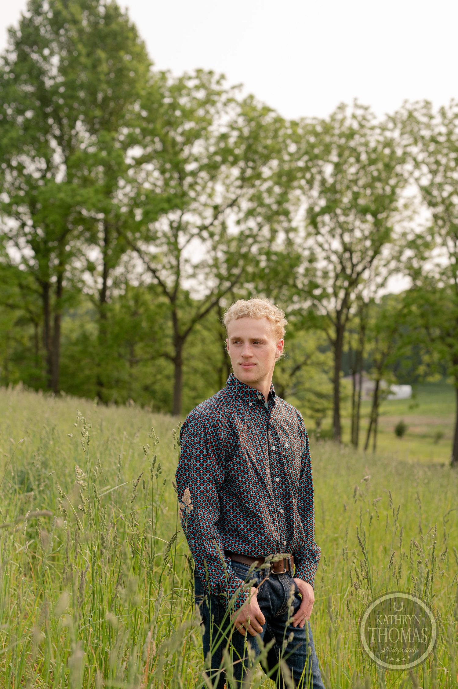 Portrait in natural meadow setting with scattered trees and tall grass.