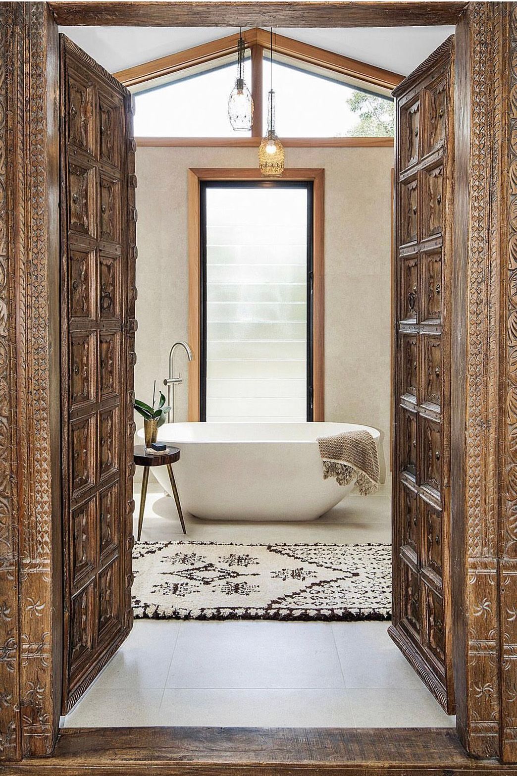 Luxurious bathroom entrance with ornate wooden doors and freestanding tub.