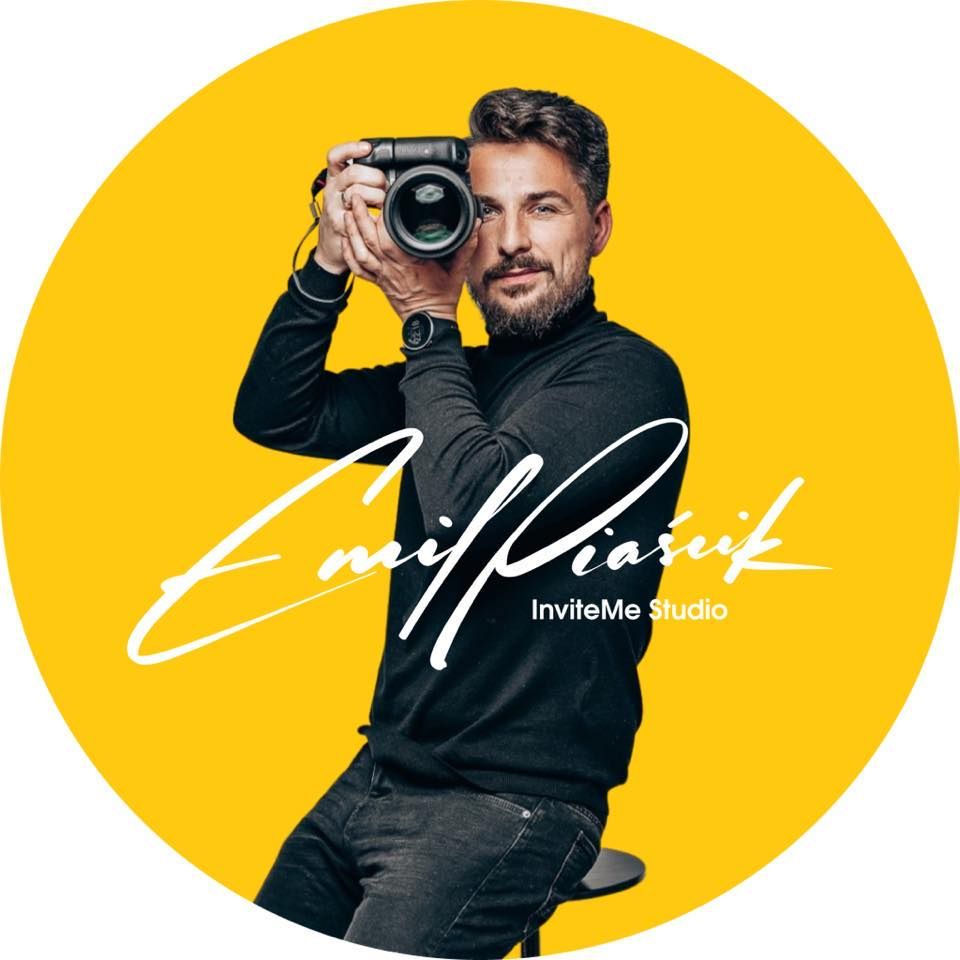 Professional photographer in black clothing holding a camera against vibrant yellow background.