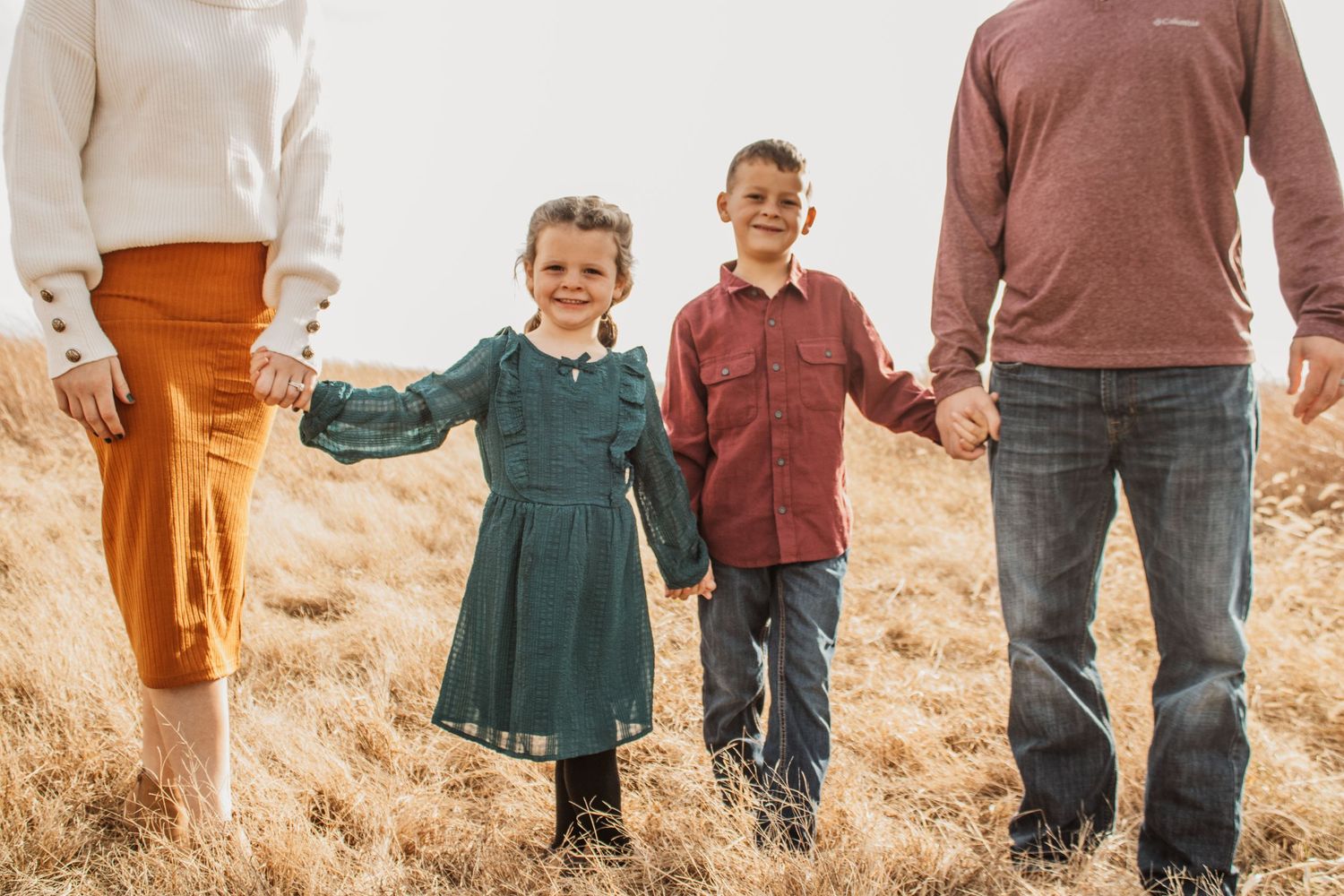 family of 4 walking towards the camera holding hands, the image is focused on the two children in the middle