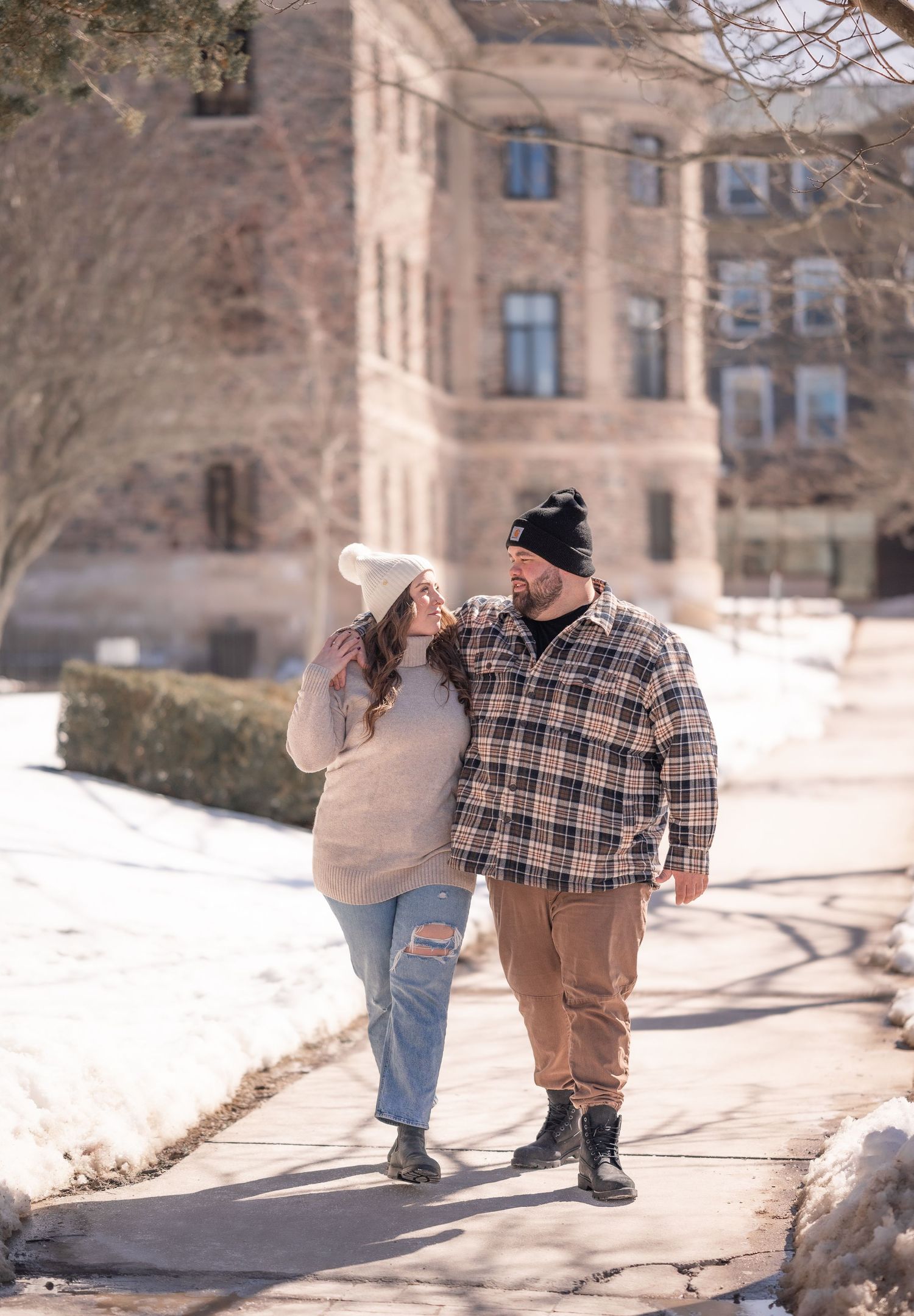 Couple walking with his arm over her shoulder during the winter amongst historic buildings in halifax.