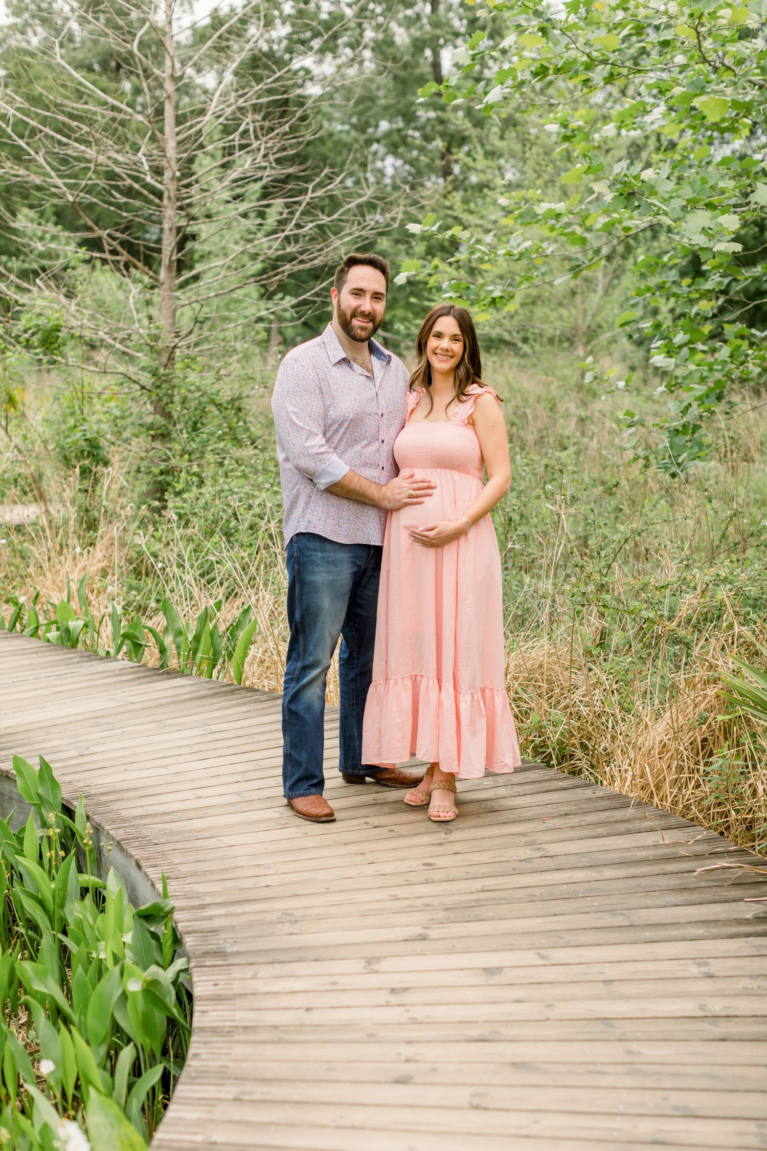 A couple poses together on a wooden boardwalk surrounded by natural greenery.