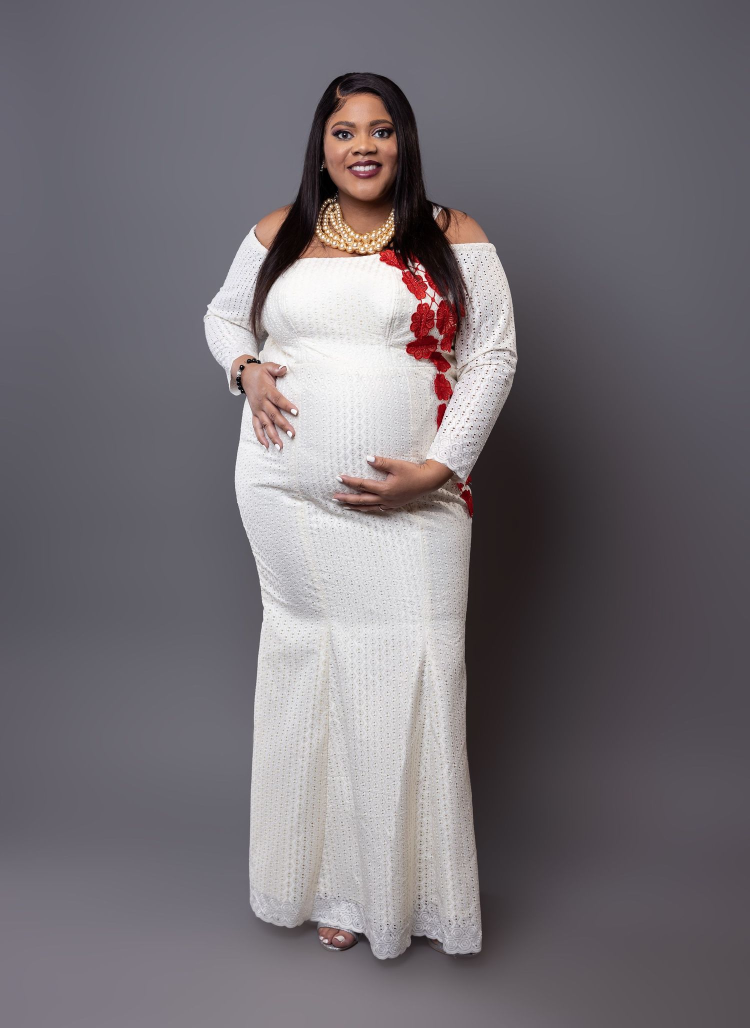Expectant mother in white sequined dress poses against gray studio background.