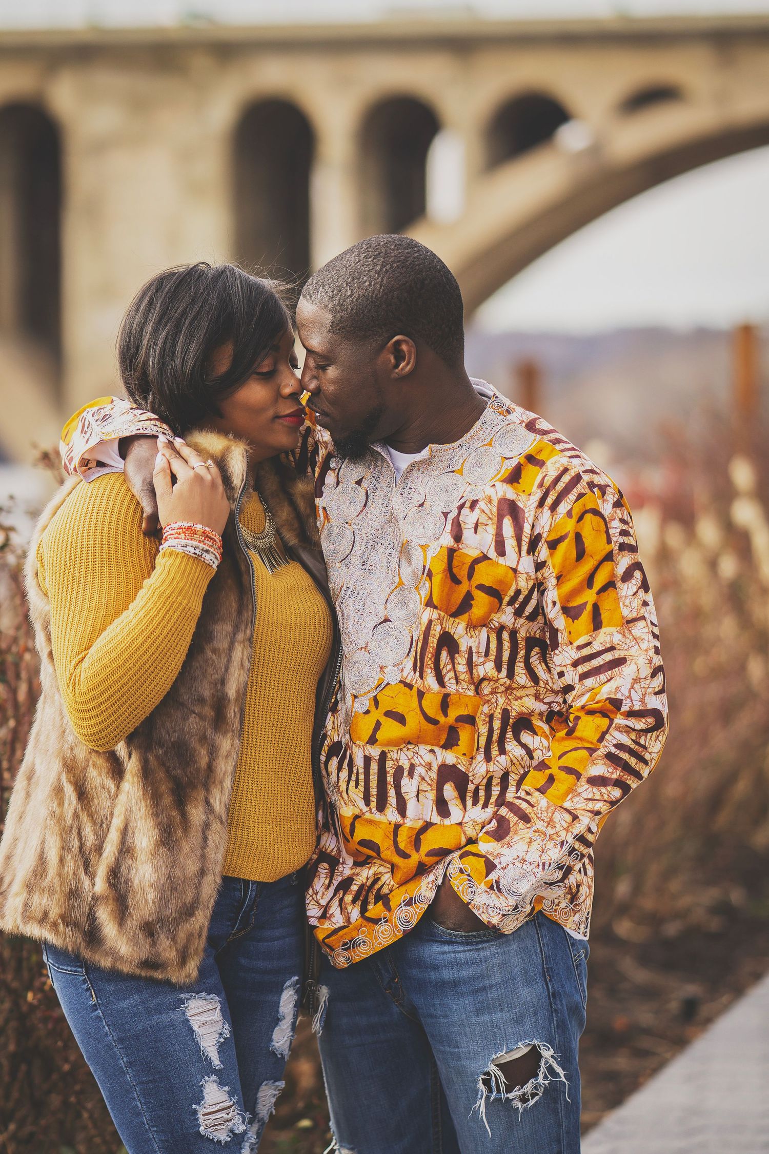 A couple in casual winter wear sharing an intimate moment near a bridge.