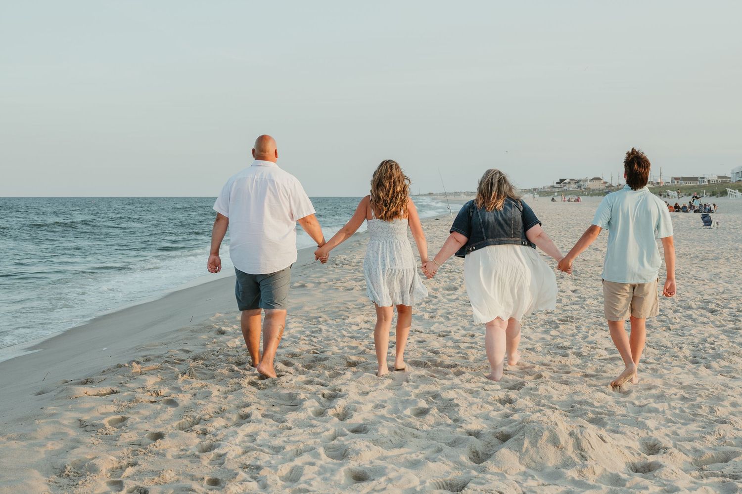 Four people holding hands while walking along the beach at sunset.