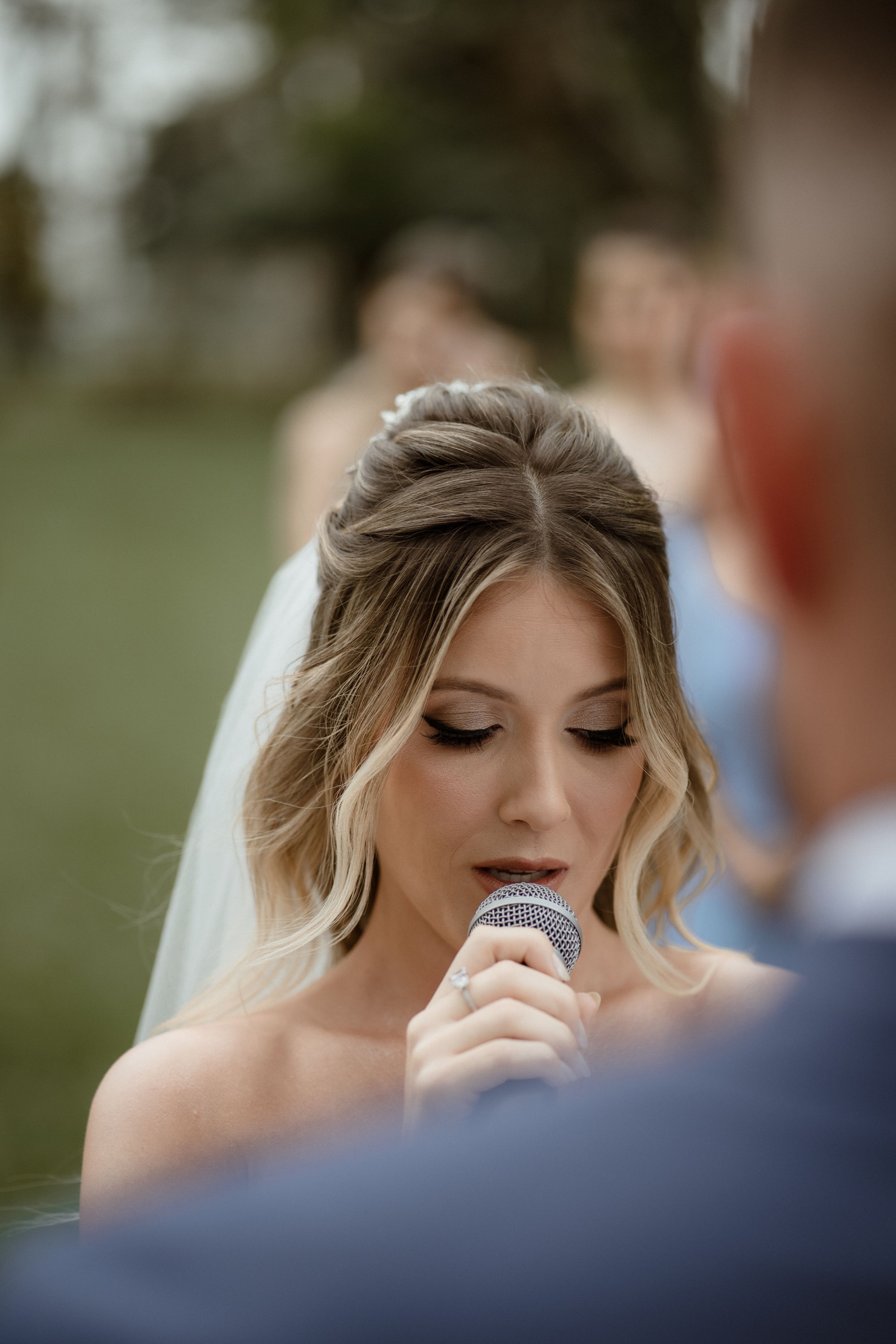 A bride in white reading vows during an outdoor wedding ceremony.