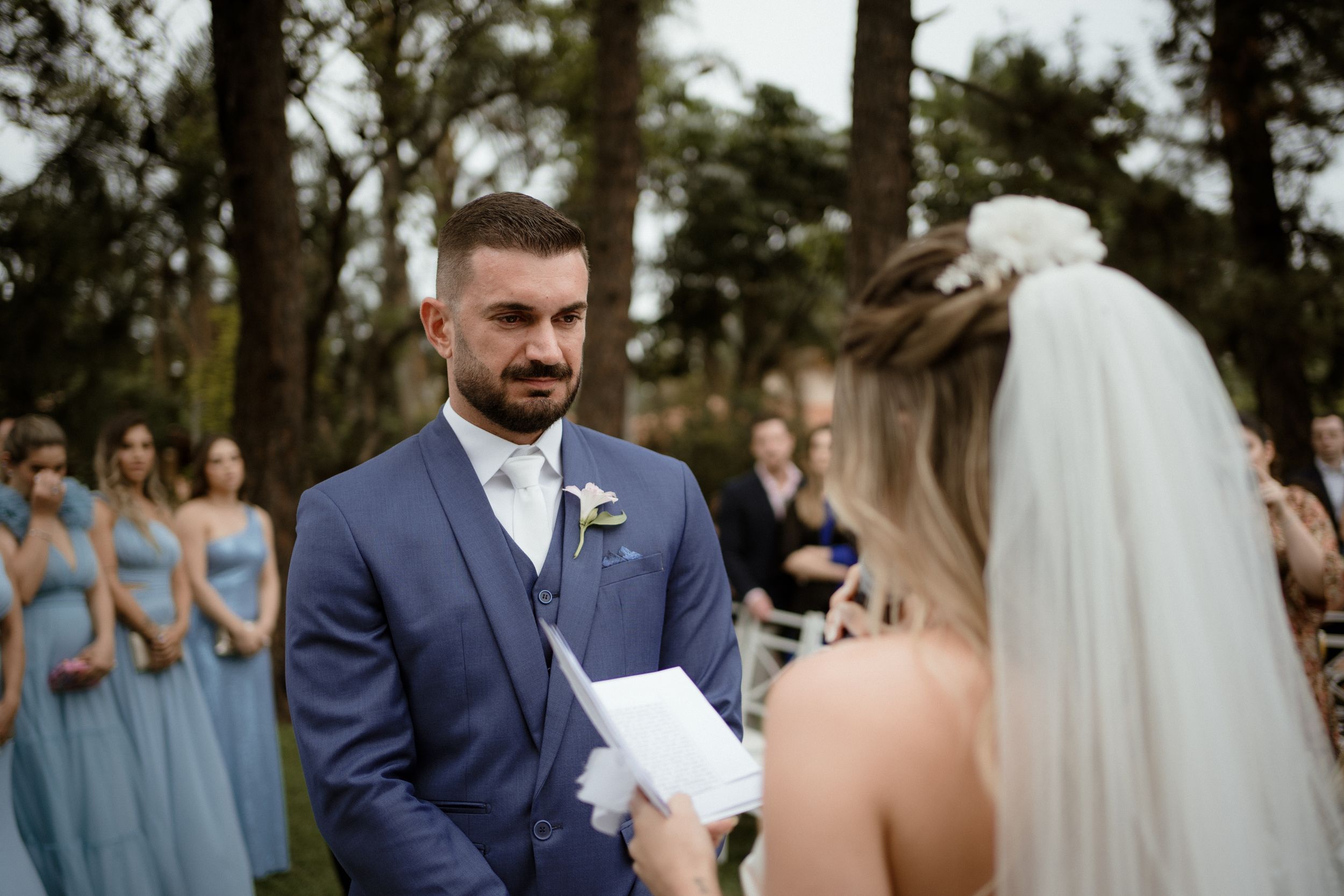 An emotional outdoor wedding ceremony with attendants in blue dresses watching.