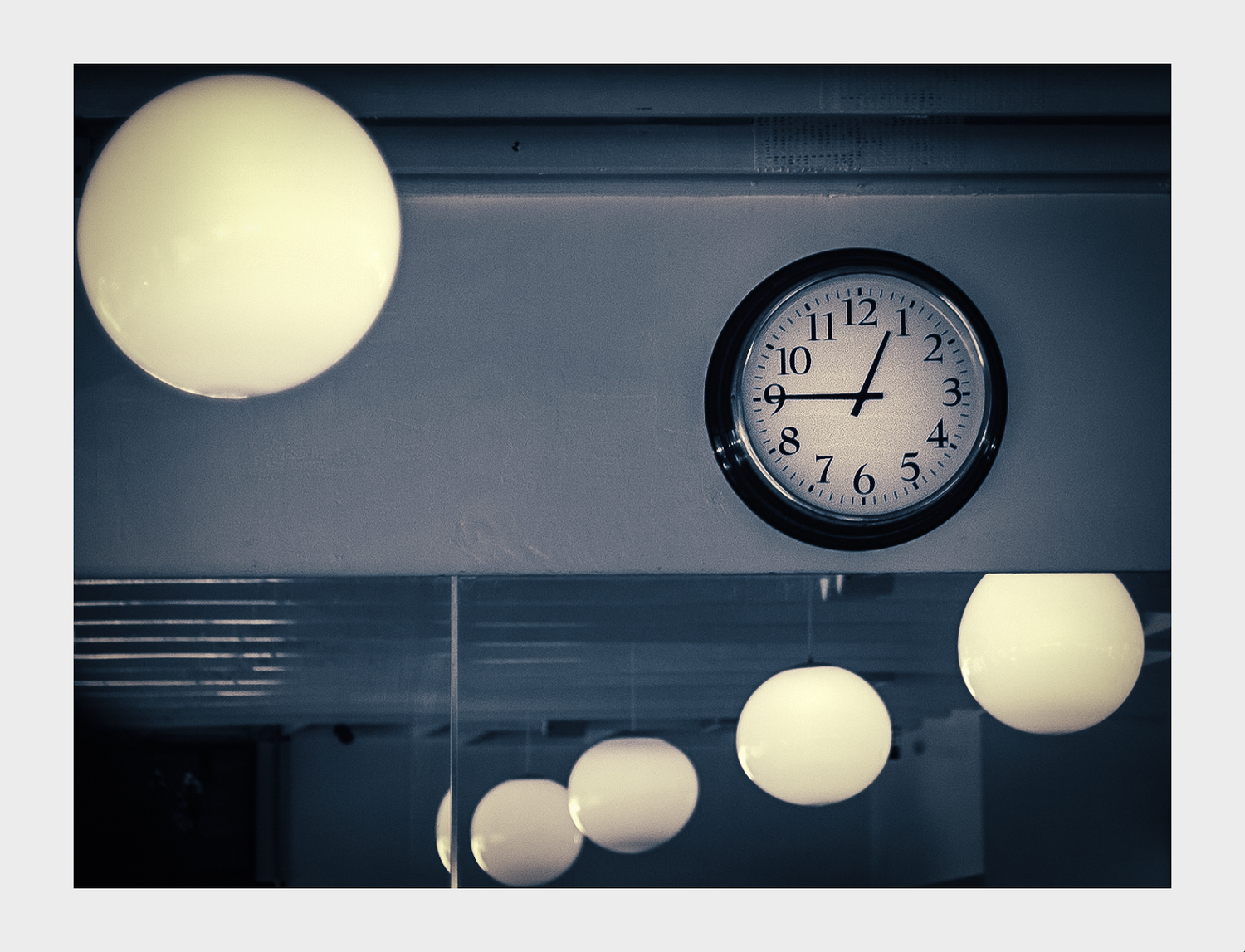 Wall clock showing 12;45PM, surrounded by globe ceiling lights and a mirror in the background.