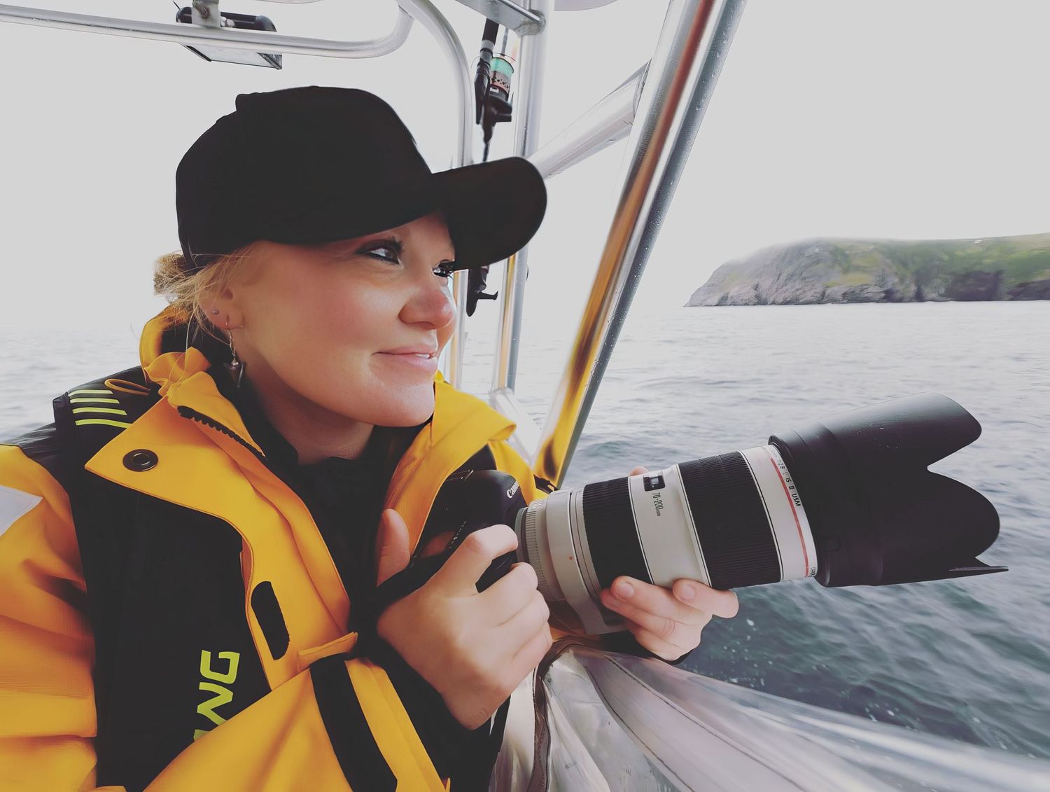 A photographer in yellow safety gear using a telephoto lens on a boat.