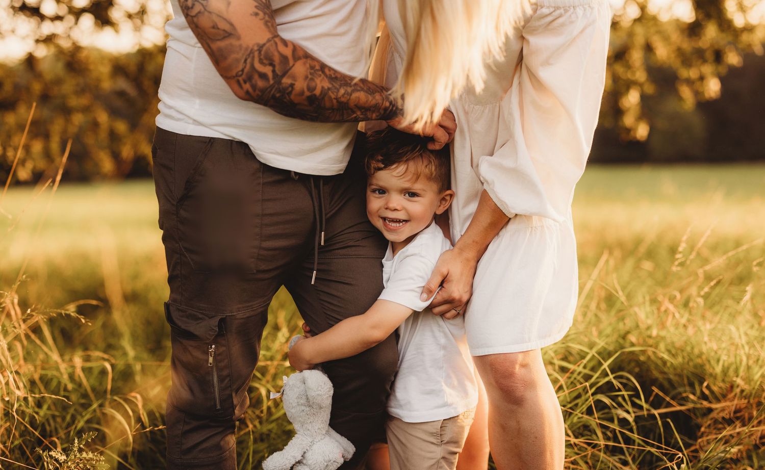 Family embracing in golden sunlit field during sunset.