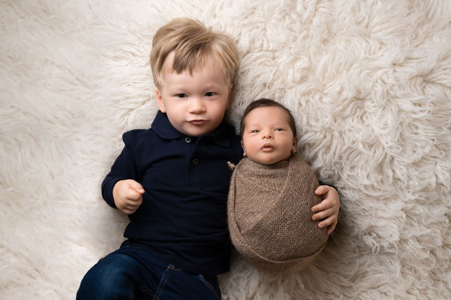 Two young children cuddling on a fluffy white rug during a portrait session.