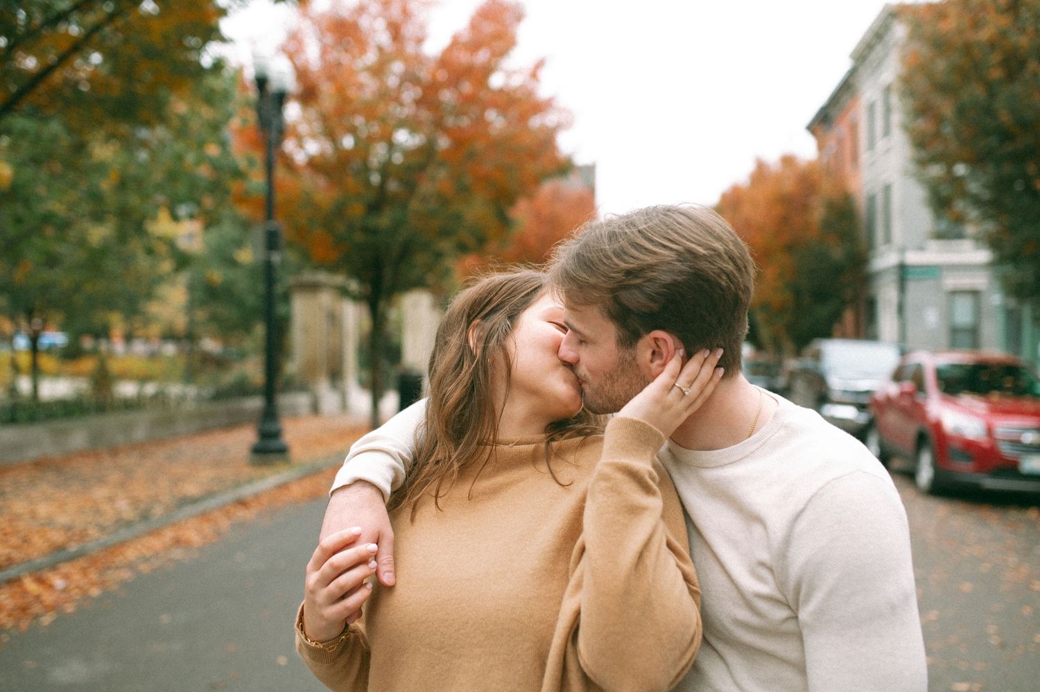 A romantic autumn scene on a leaf-covered street with fall foliage in the background.
