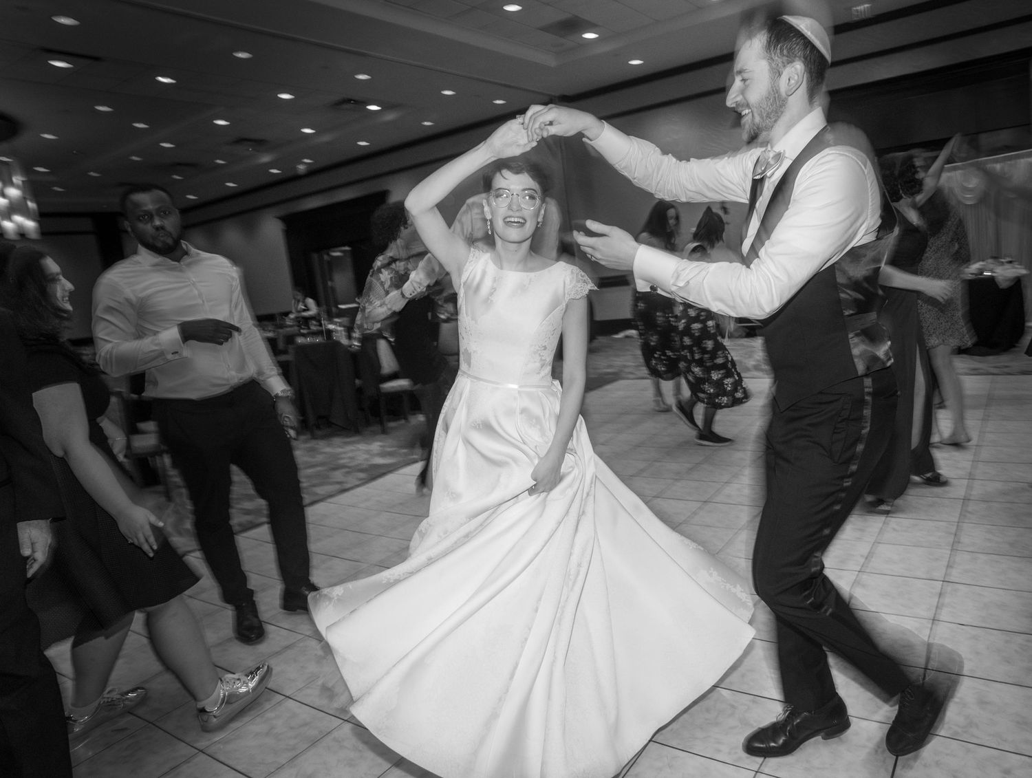 A couple dances joyfully on the reception dance floor in black and white photography.