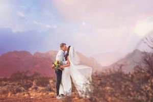 Wedding couple poses against red mountains with flowing veil in desert sunset.