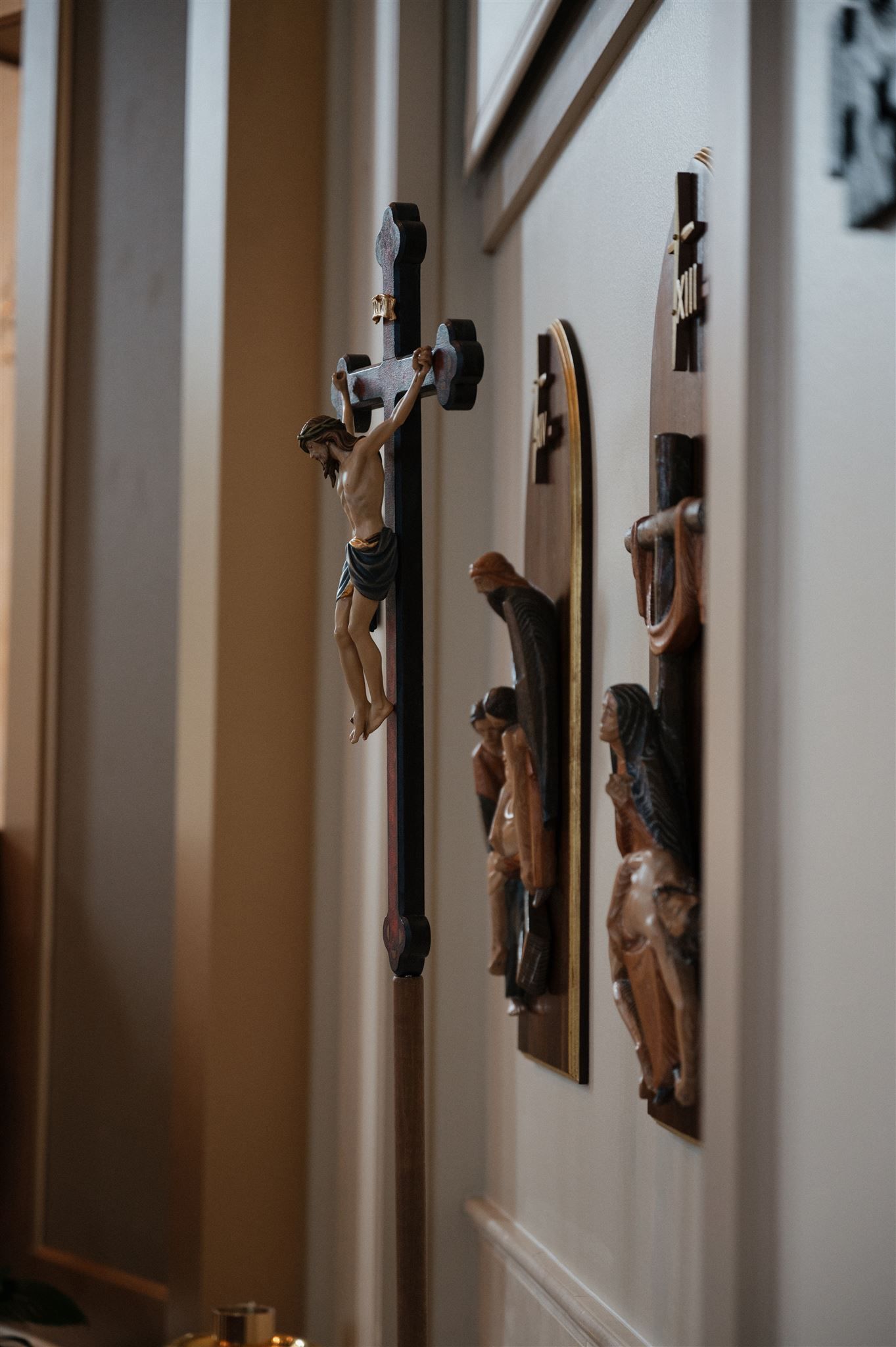 Religious wall art featuring crucifixes and wooden carvings mounted on white church walls.