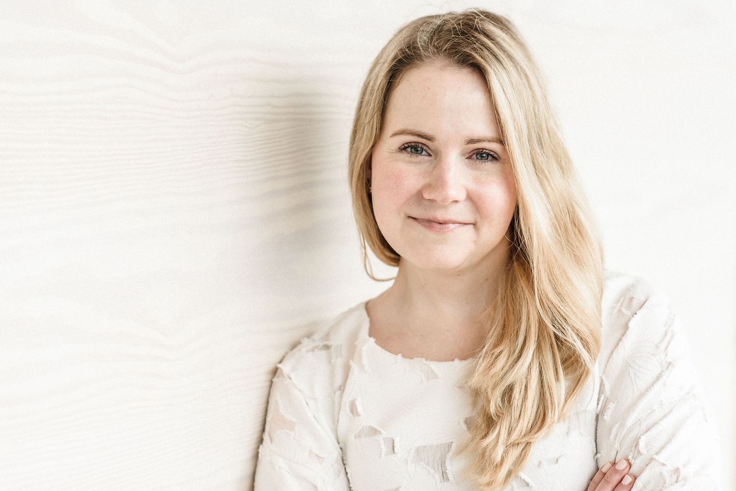 Portrait of a blonde woman in white against a light background.