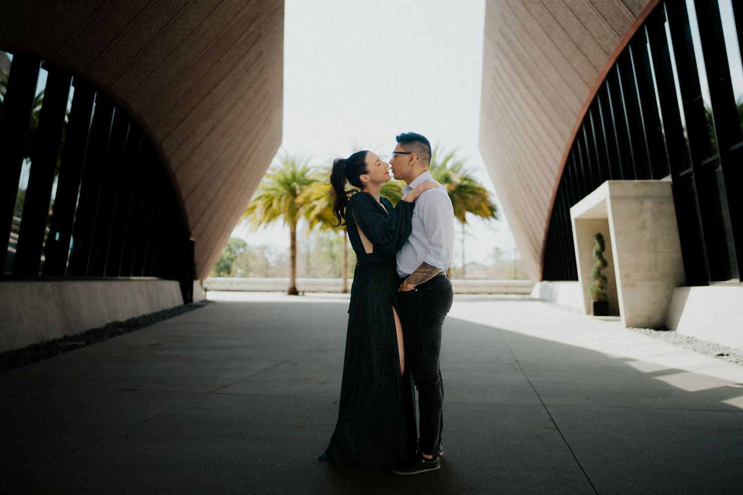 A romantic couple shares an intimate moment under a modern architectural archway.