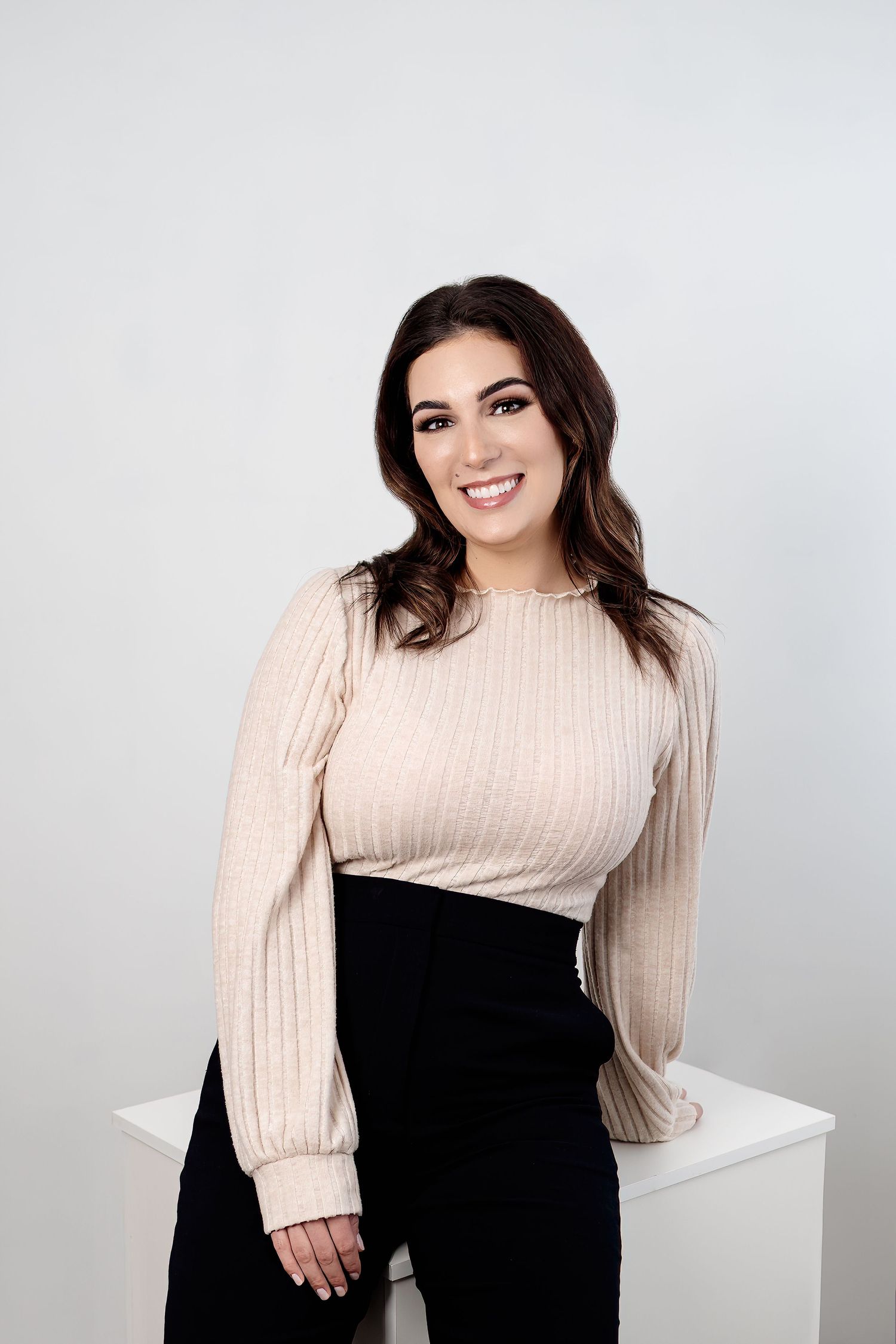 Portrait in cream ribbed sweater and black skirt against minimalist white backdrop.