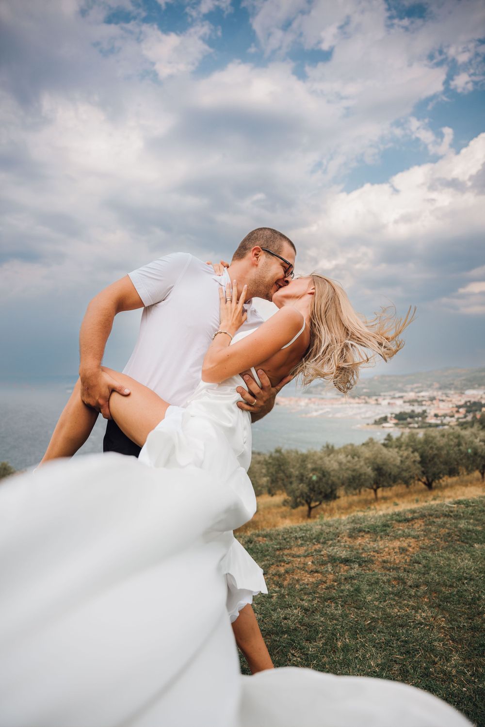 Romantic wedding couple embracing in a sunlit meadow with mountains in background.