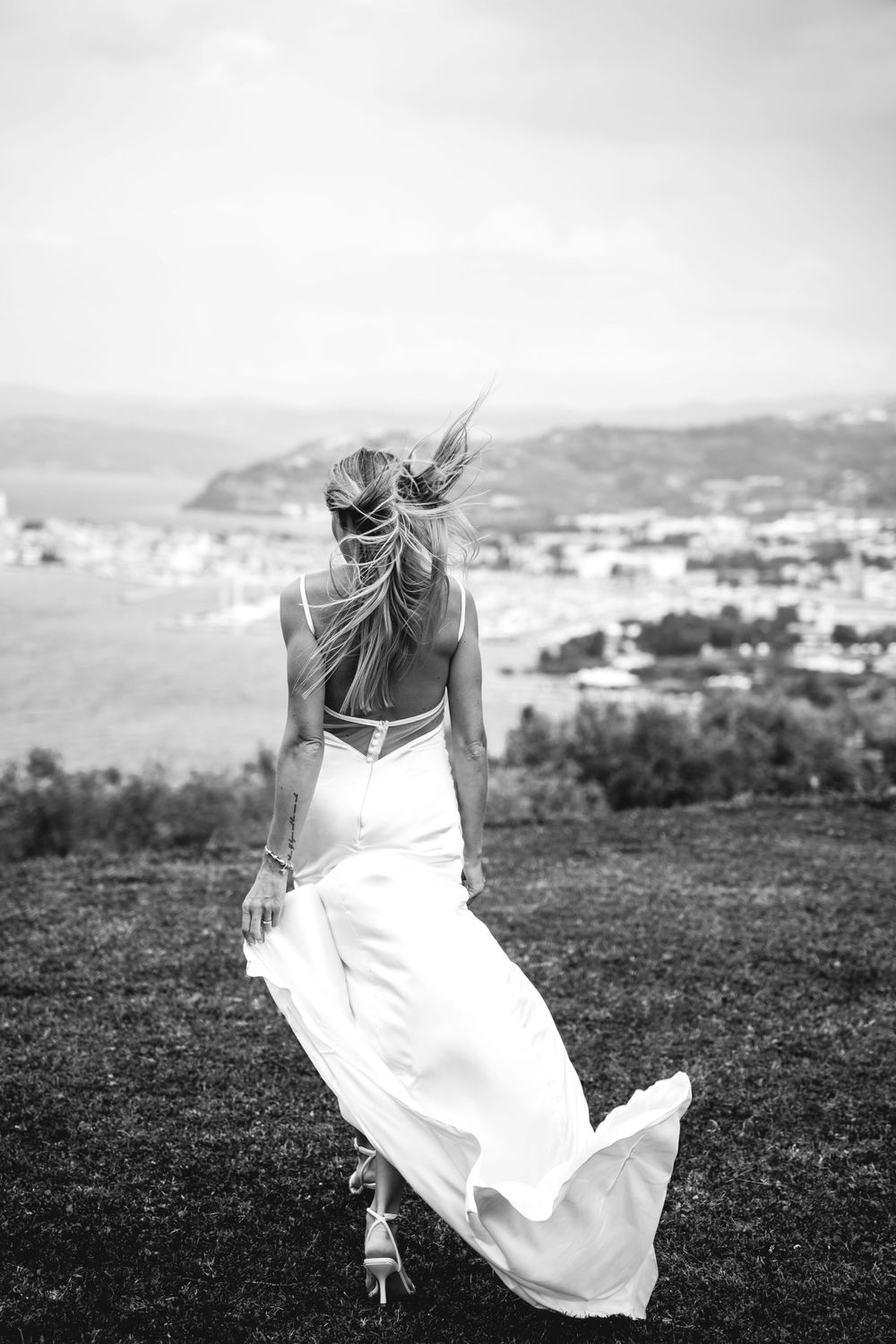 Black and white portrait of flowing dress movement against a hillside landscape.
