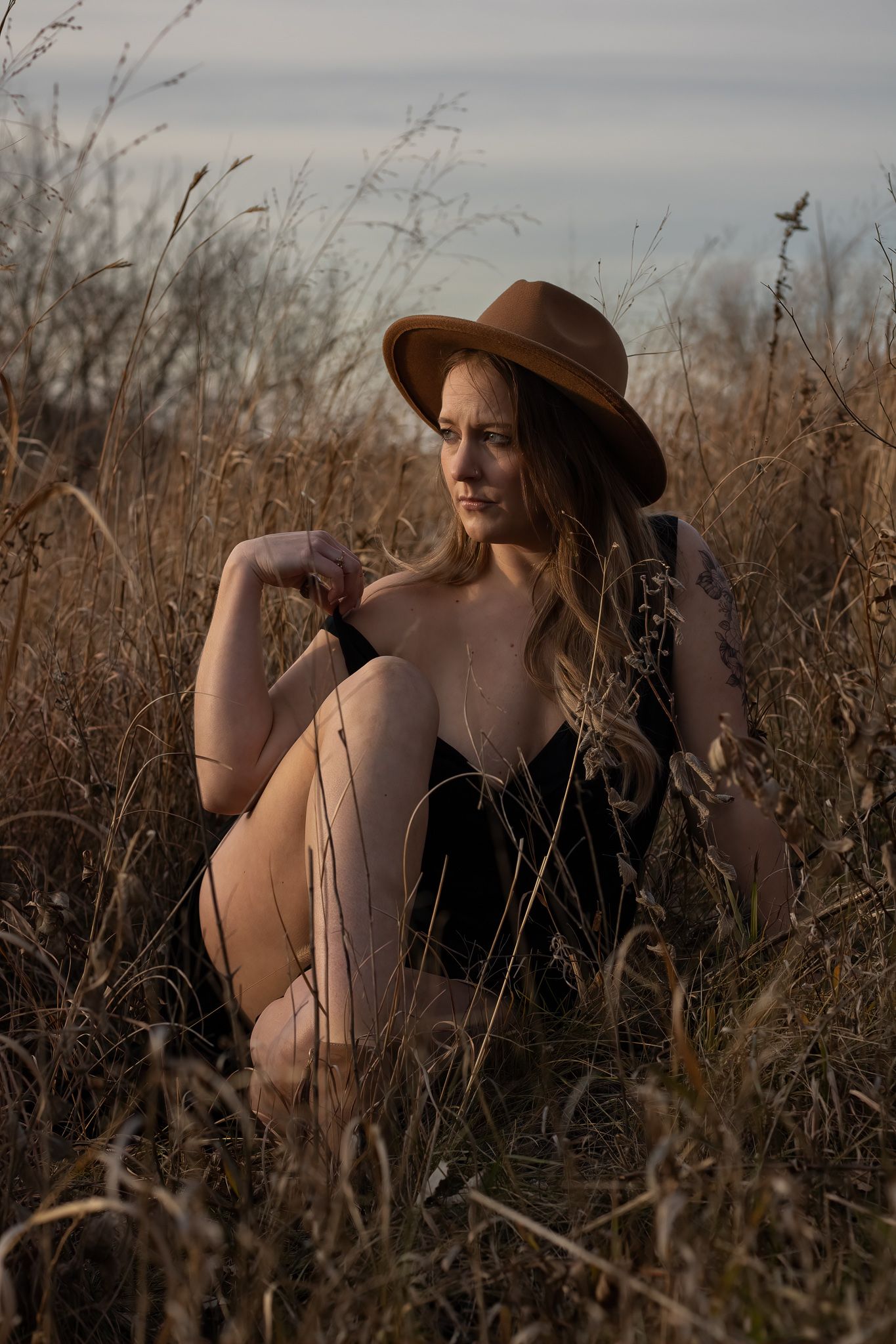 Artistic portrait in tall grass at sunset with brown hat and natural lighting.
