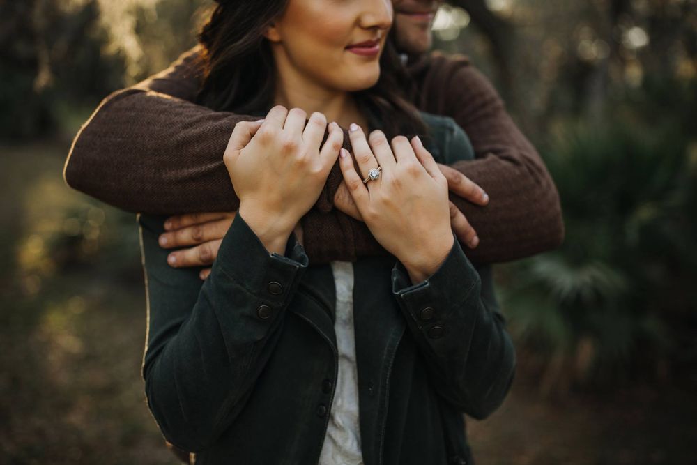 Woman holding the arm of her fiance in a field in Sarasota, Florida at their engagement session.