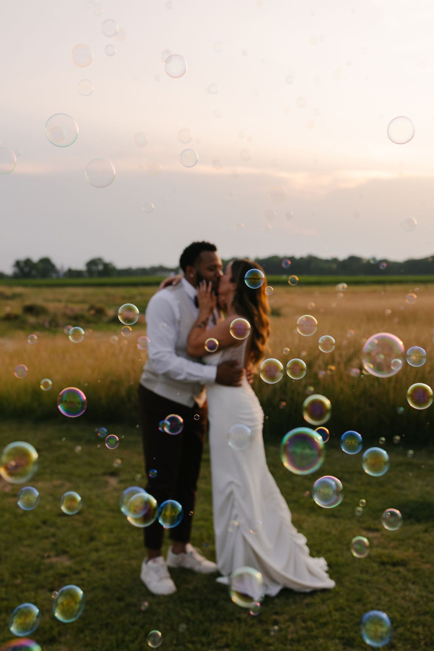 Newlyweds playing with bubbles in a golden field during sunset.