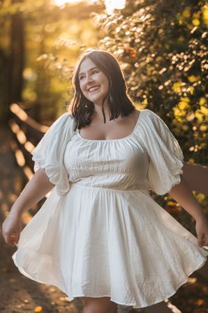 Magnificat senior exudes grace and joy as she playfully adjusts her dress, casting a charming smile away from the camera