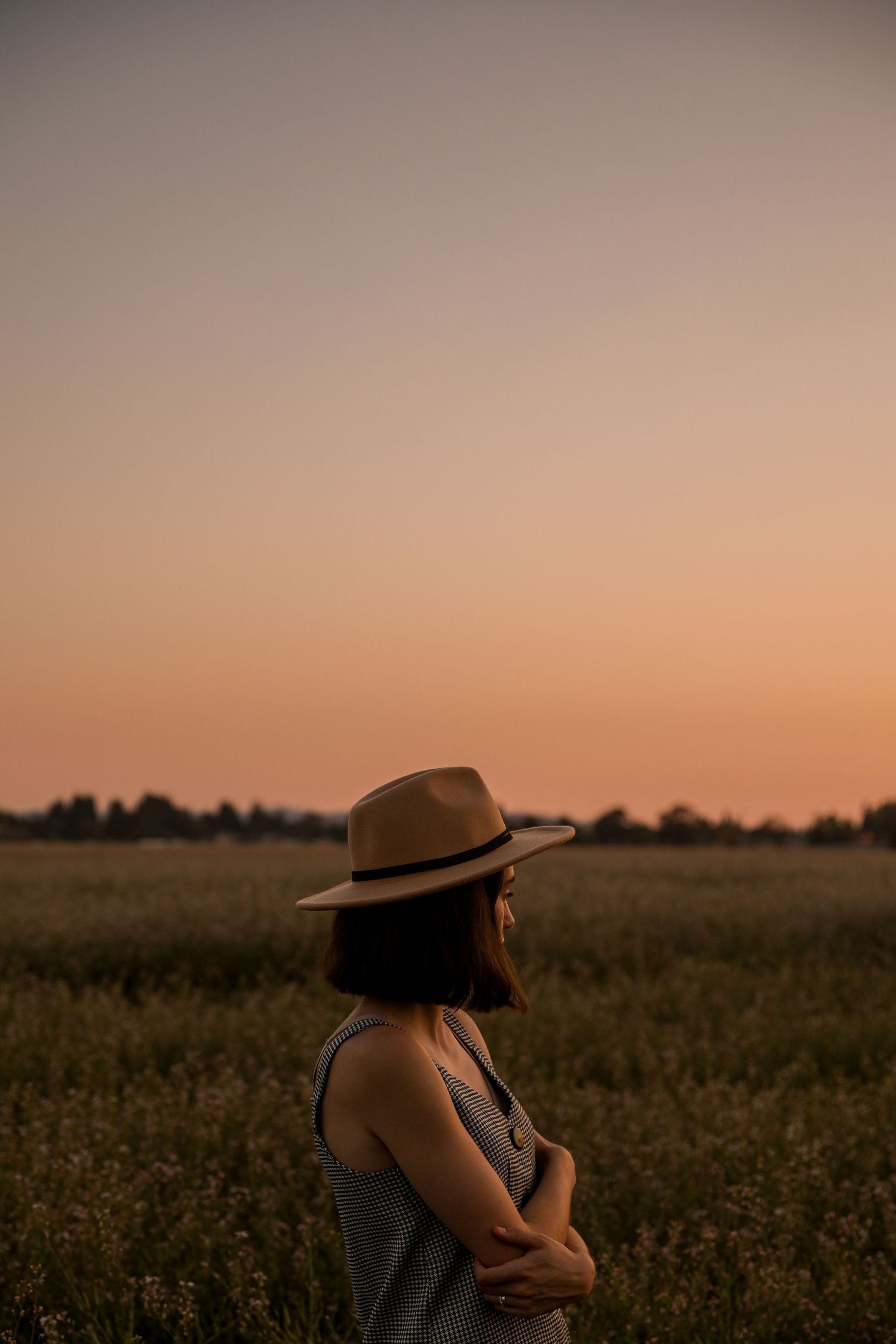 Silhouette against pink sunset sky wearing hat while standing in wildflower meadow.