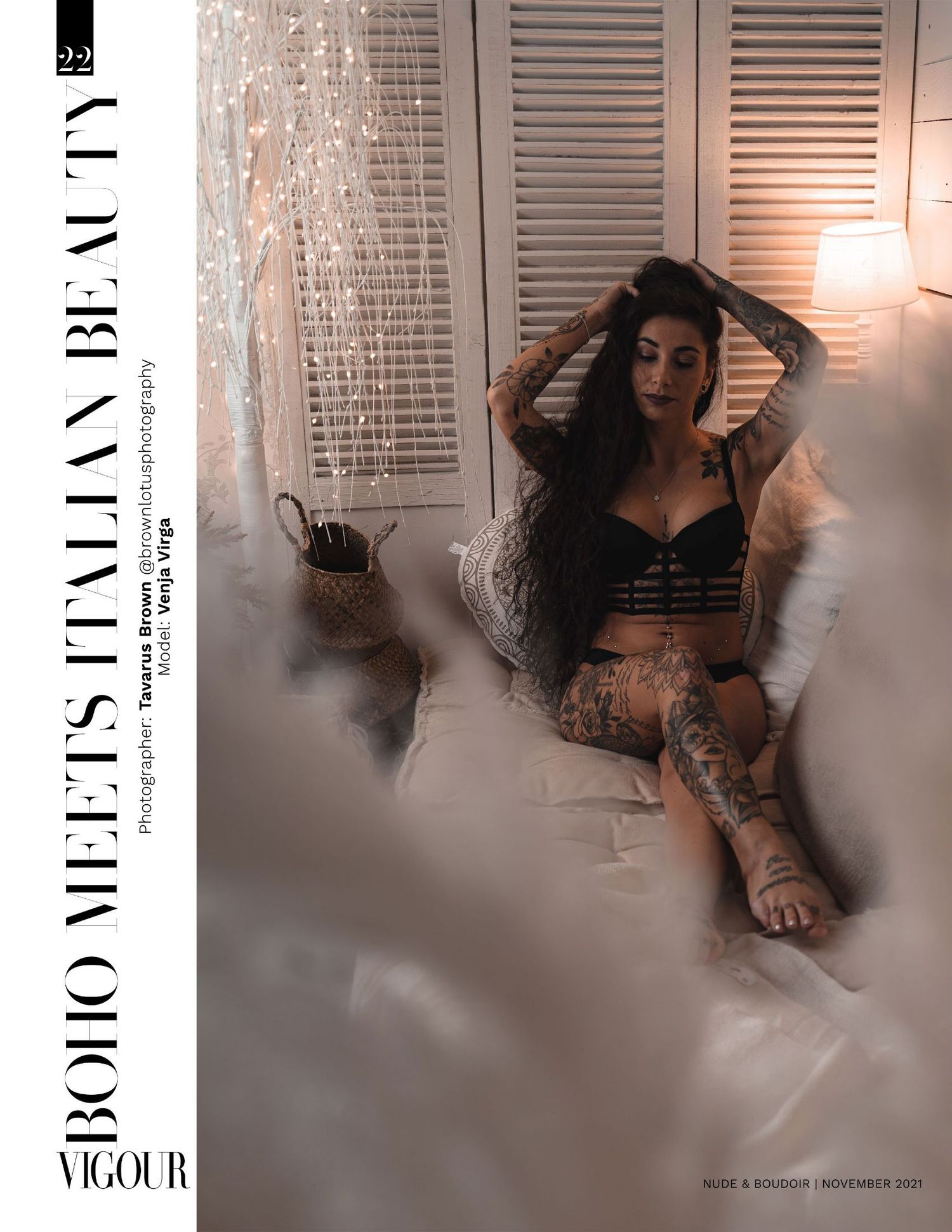 An atmospheric boudoir photo shoot with moody lighting features a tattooed woman sitting by white shuttered windows.