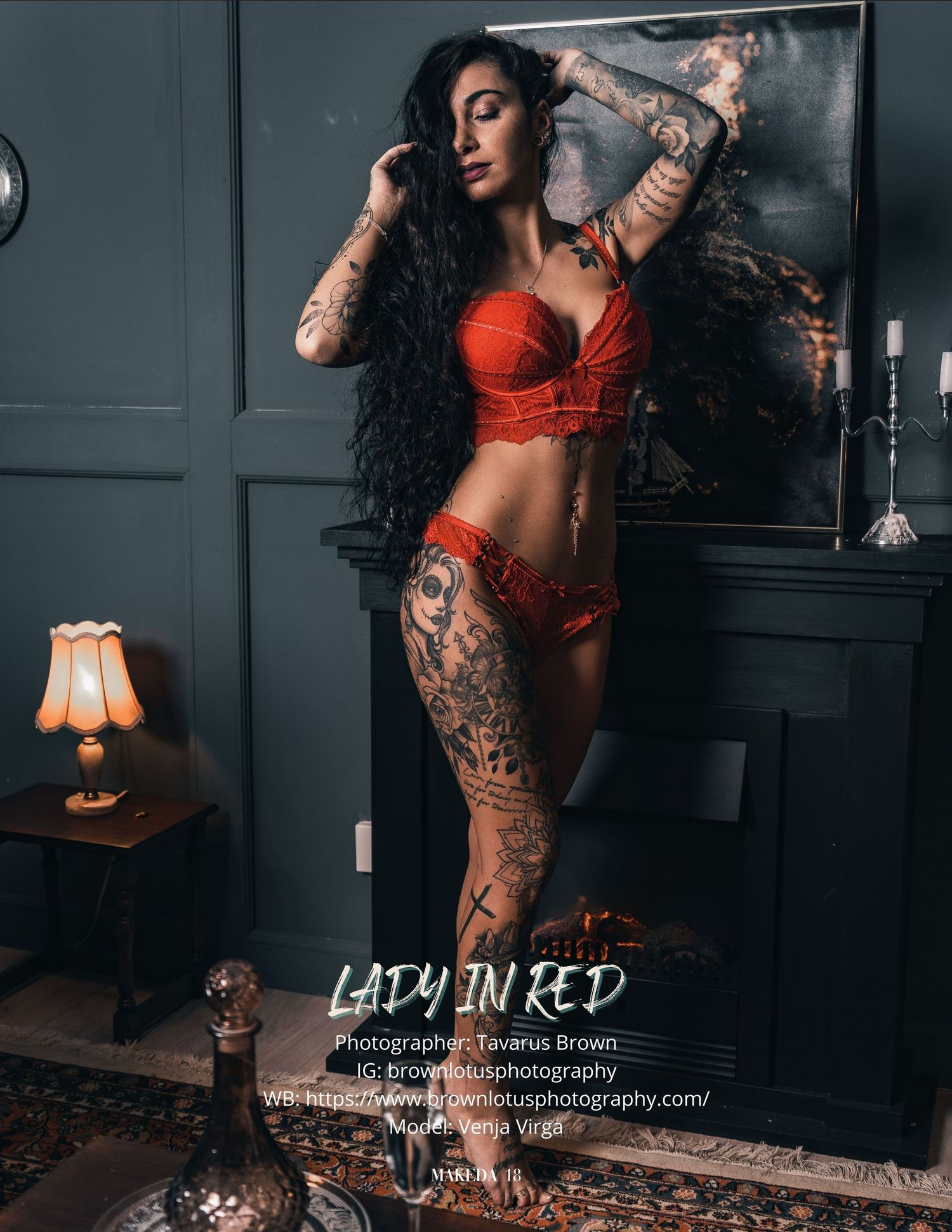 A model in red lingerie poses dramatically against a dark wall with tattoos and vintage lamp decor, creating a moody ambiance.