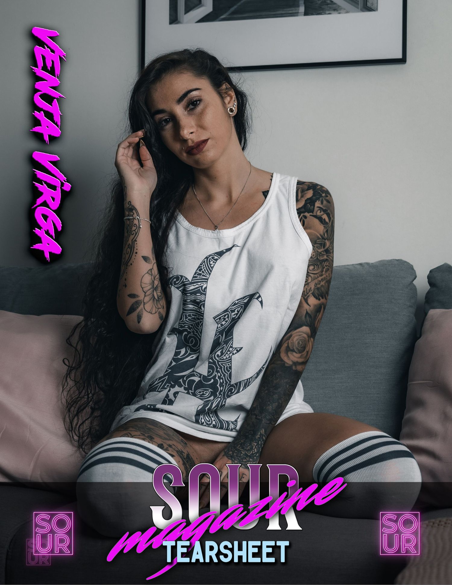 Alternative model in white tank top with tattoos posing on grey couch.