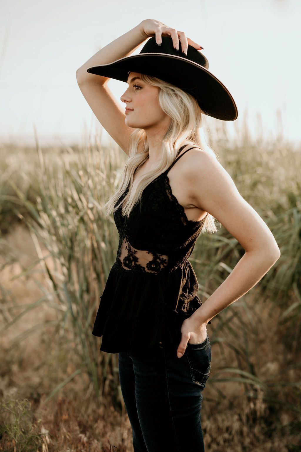 girl standing in tall grass holding her western style hat