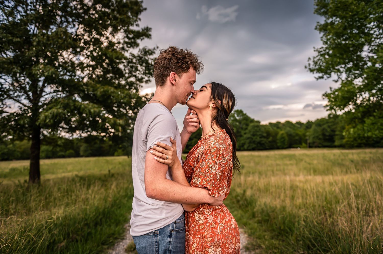 Engagement photos taken on a tree-lined path in a romantic summer field setting.