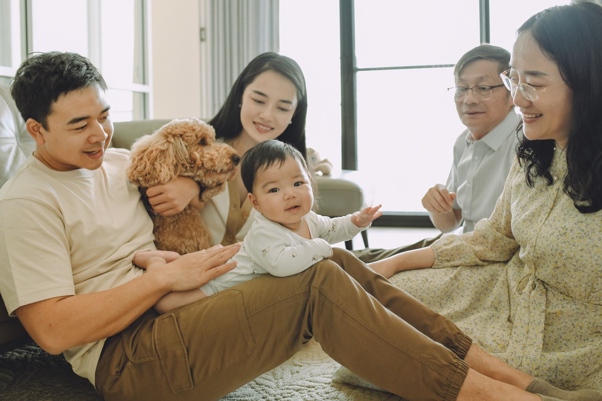 A family plays with a fluffy brown toy dog while relaxing together on a couch in a bright room.