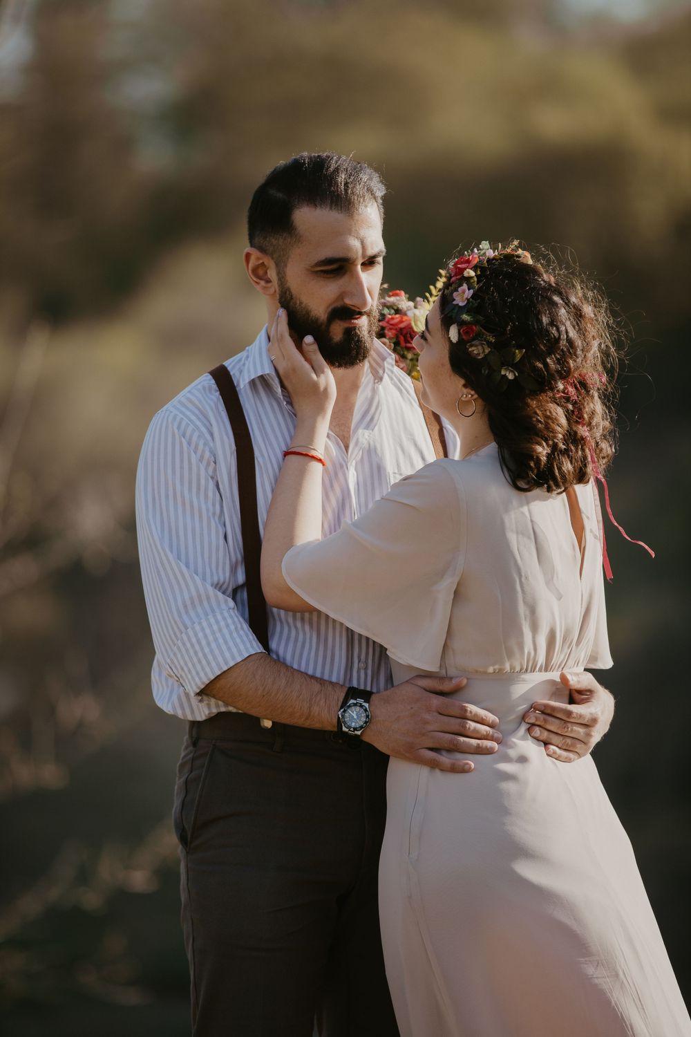 A romantic couple embraces outdoors in vintage-inspired wedding attire against a natural backdrop.