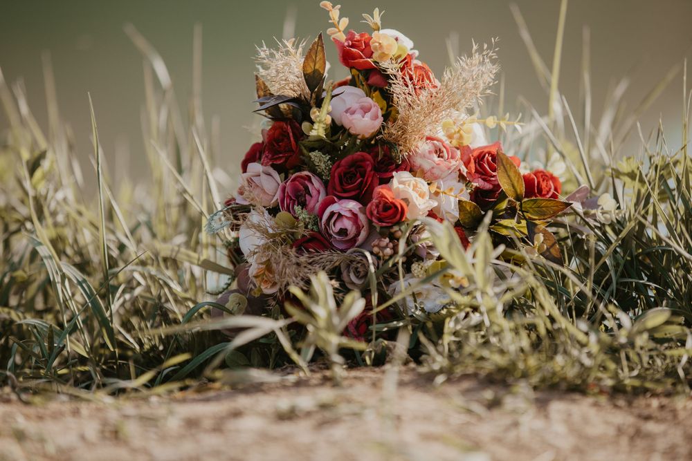 A wedding bouquet with roses and dried flowers rests in sunlit grass.