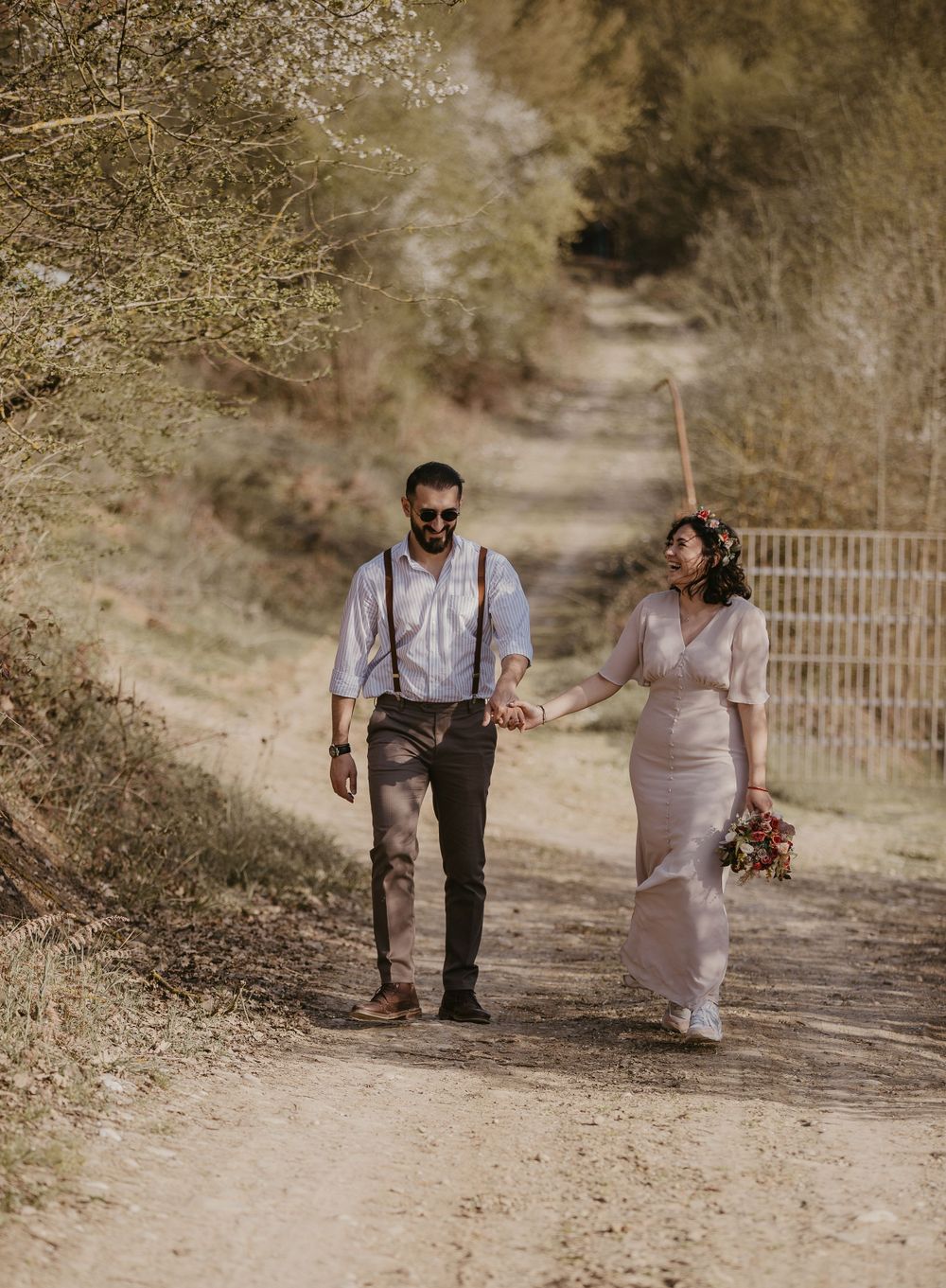 A couple walks together on a scenic trail wearing vintage-inspired wedding attire.