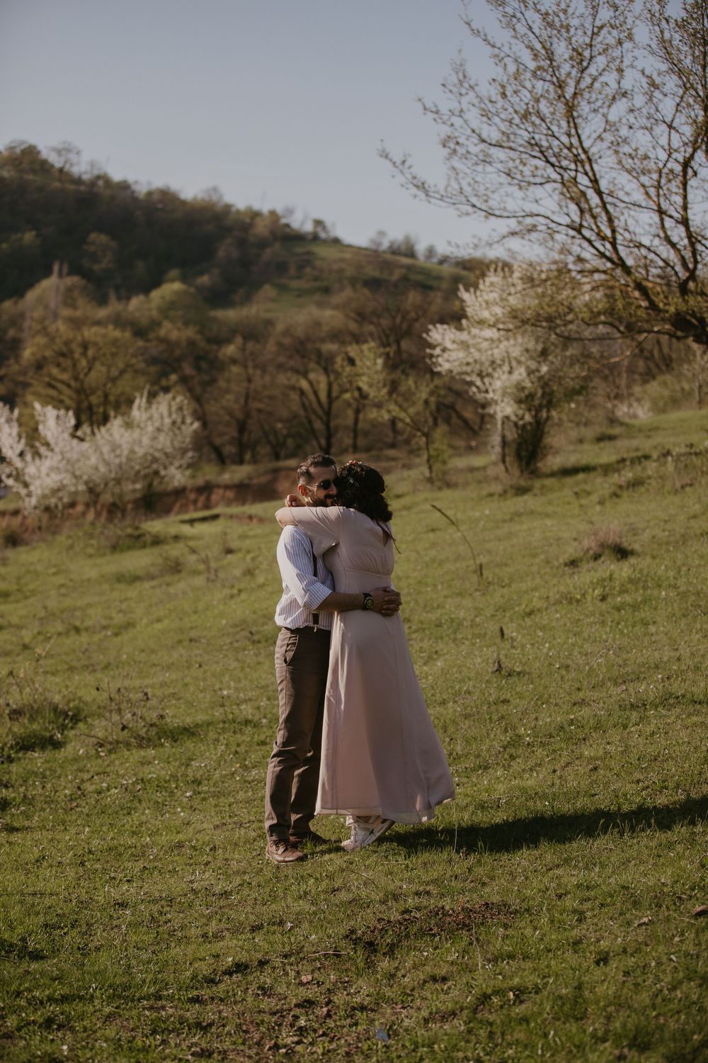 A romantic embrace on a hillside with blooming spring trees in the background.