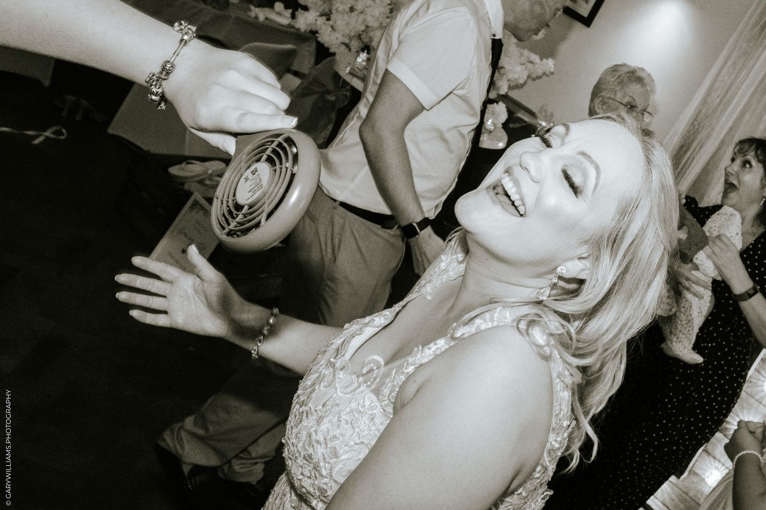 Black and white photo of a bride being fanned by a wedding guest at her reception after her Christian wedding in London