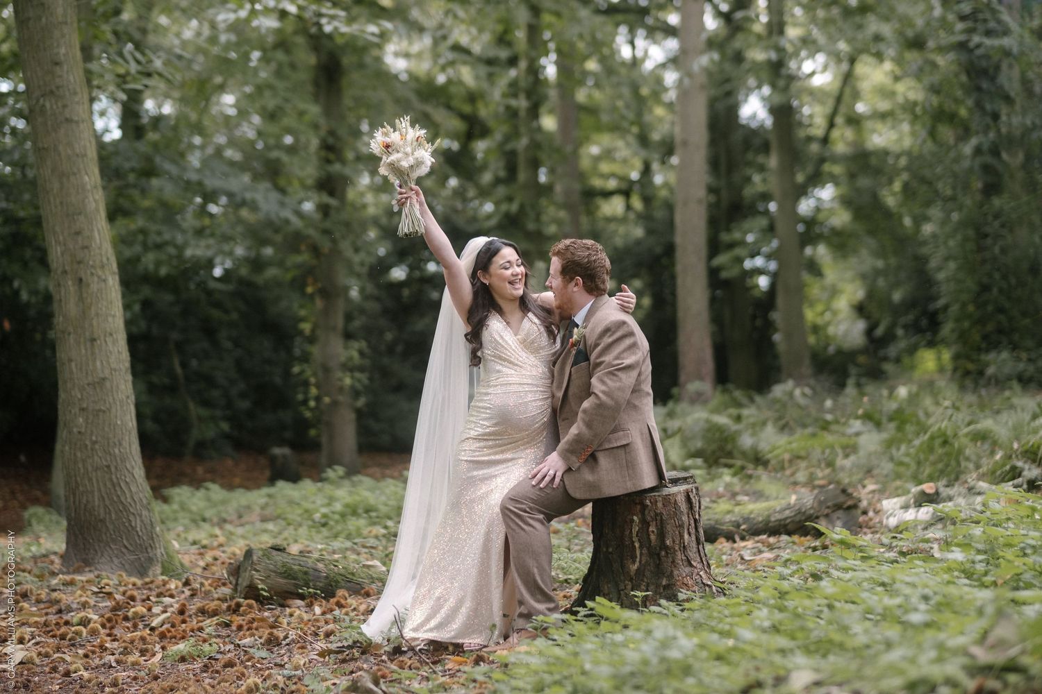 Newlywed bride and groom seated together on a stump in the woods after their wedding at Amphill Registry Office Wedding