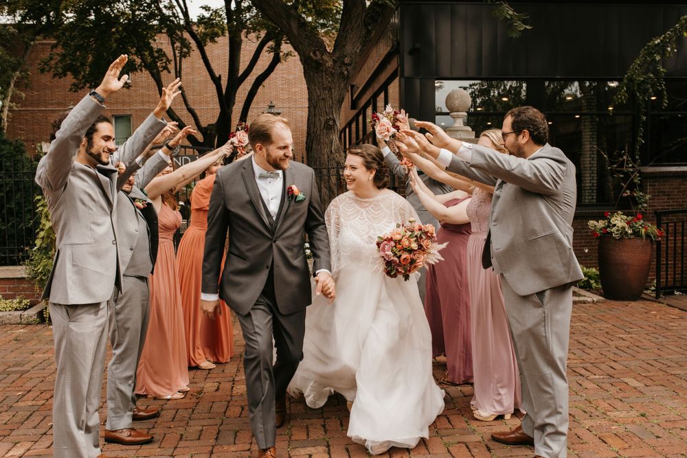 Bride and groom walk through tunnel of raised hands formed by cheering wedding party.