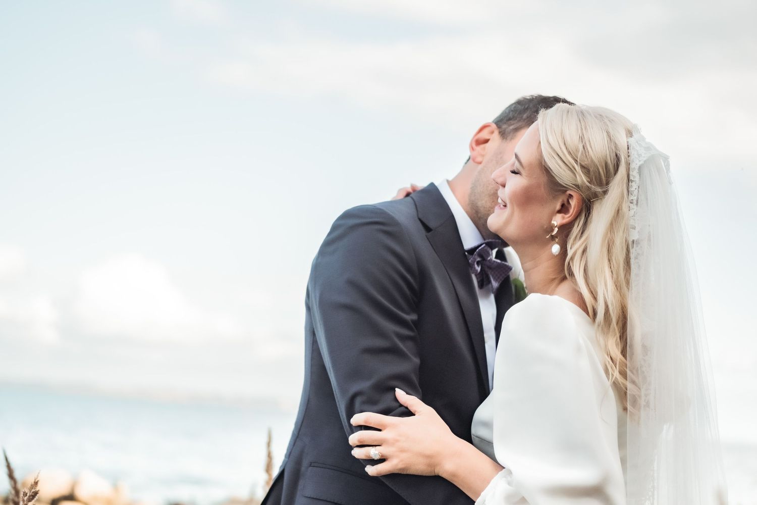 Couple shares intimate moment during beach wedding with ocean backdrop.