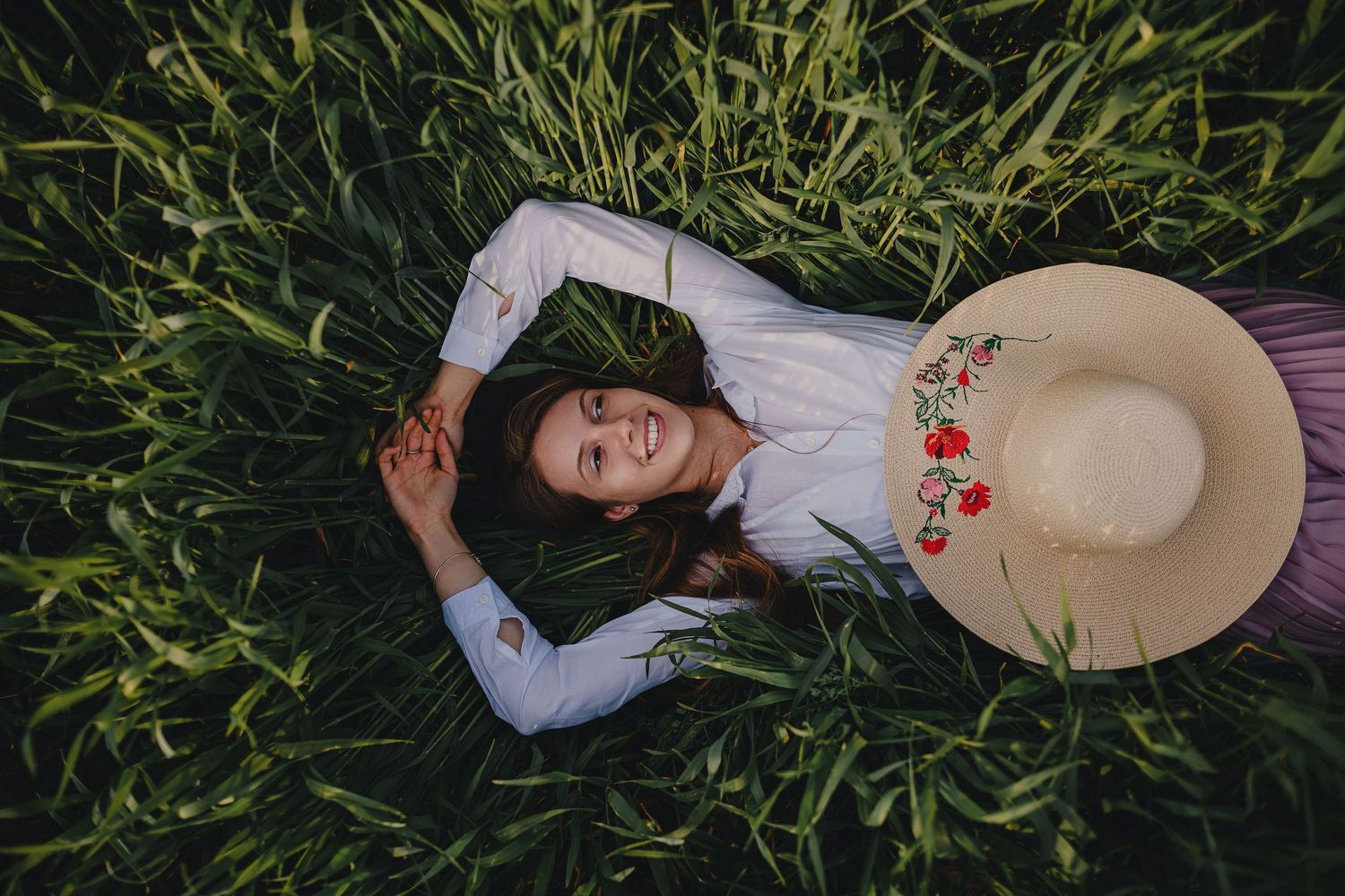 An artistic portrait of someone lying in tall grass with a sun hat.