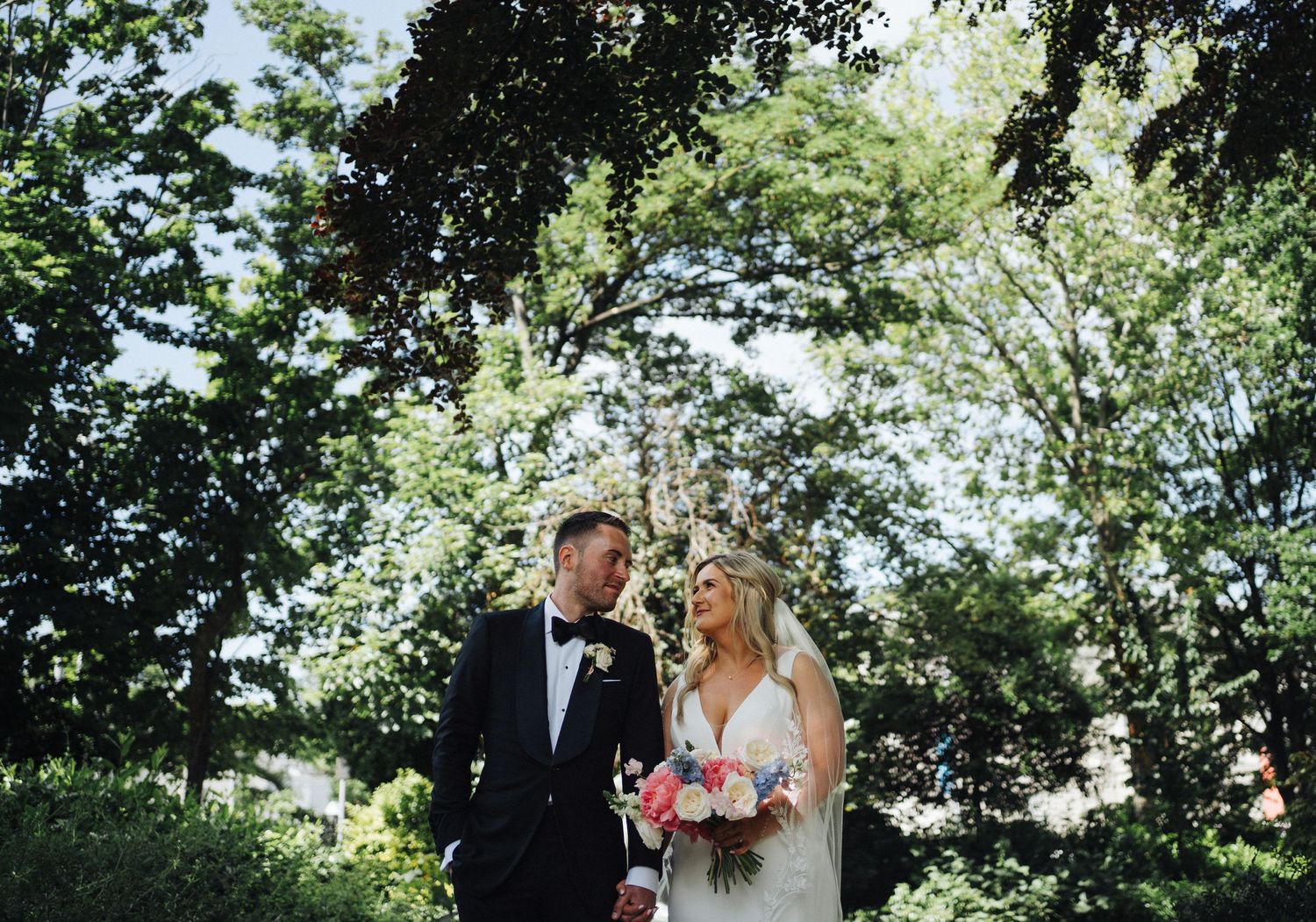 A joyful outdoor wedding portrait of a couple surrounded by lush greenery and trees on their special day.