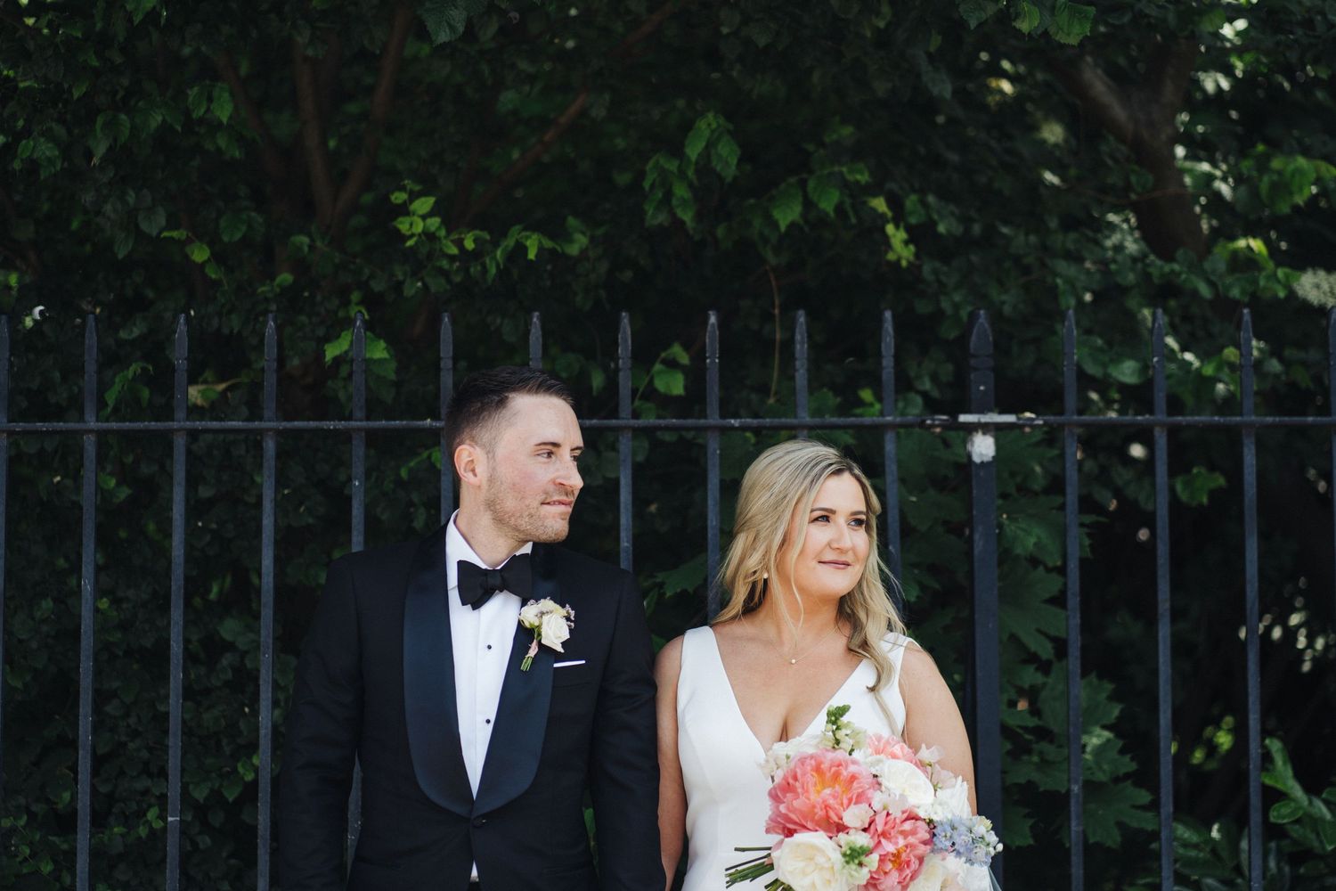 A couple shares a candid moment together by an iron fence during their wedding photoshoot.