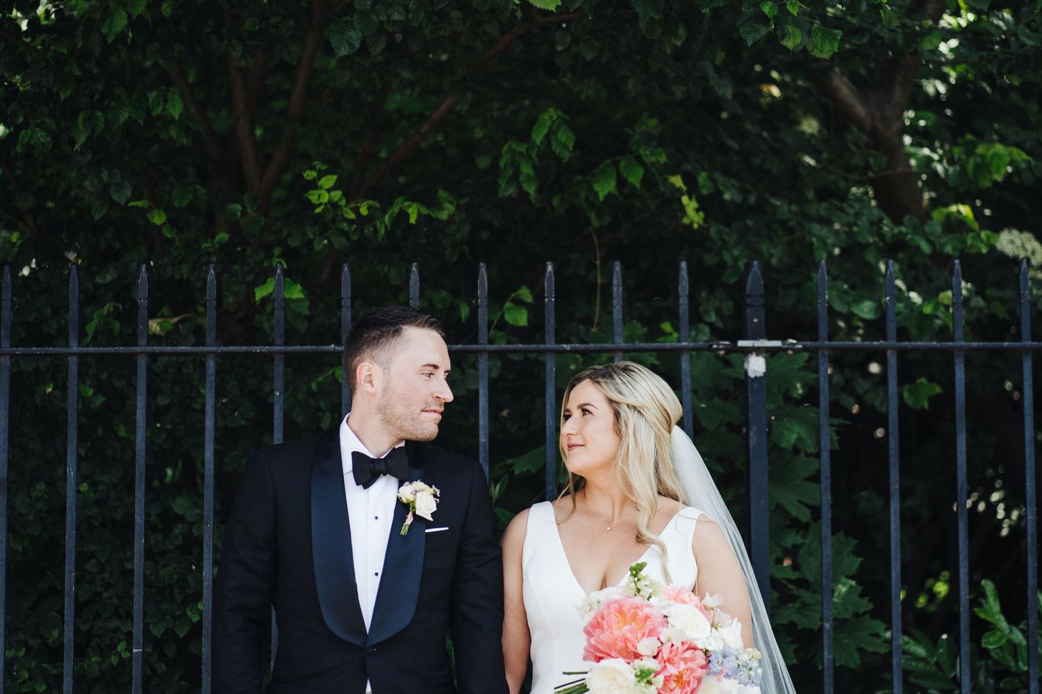 A couple laughs together during their wedding portraits by a decorative iron gate.