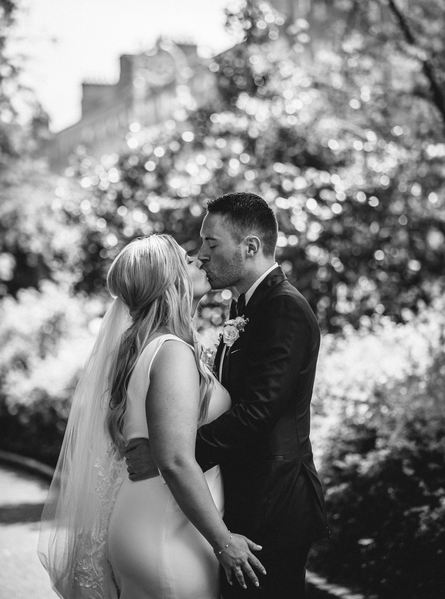 An intimate black and white portrait of newlyweds sharing a kiss outdoors.