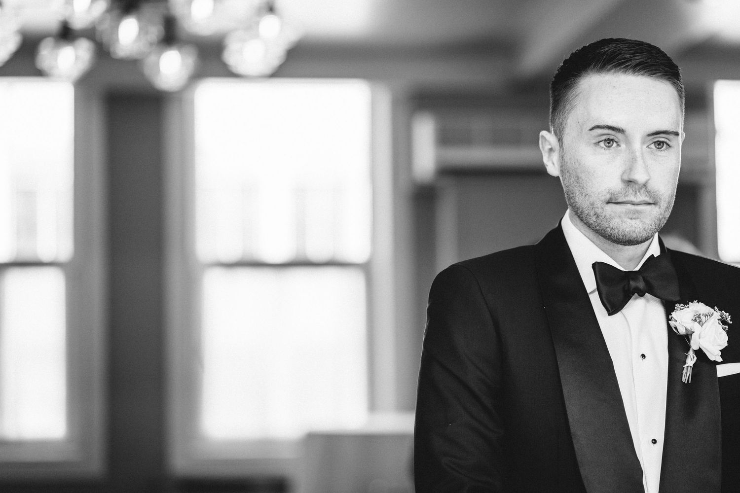 A black and white portrait of a groom in a classic tuxedo with boutonniere.